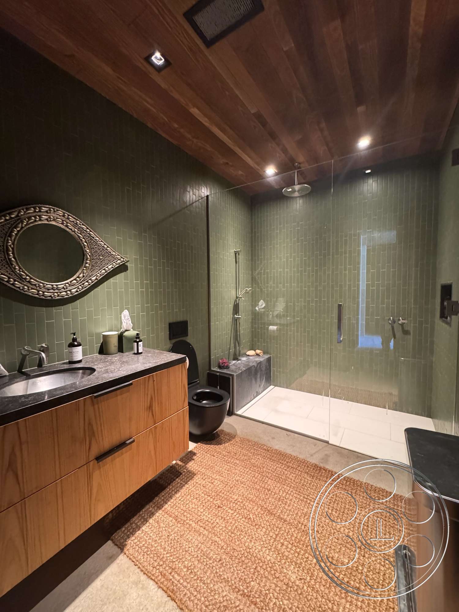 Modern 527 - glass shower enclosure, concrete bathroom flooring, decorative wall mirror, hardwood ceiling, green tile bathroom walls, stone vanity countertop, exposed wood bathroom cabinetry, freestanding black toilet, woven bathroom rug