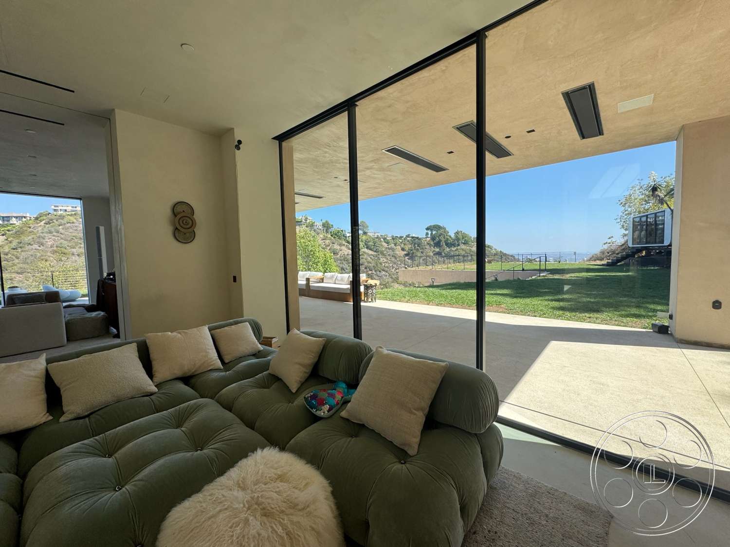 Modern 527 - exposed concrete walls, high ceiling, mountain view, open-plan living space, textured plaster wall finish, floor-to-ceiling glass windows, concrete patio floor, green tufted sofa, outdoor grass area