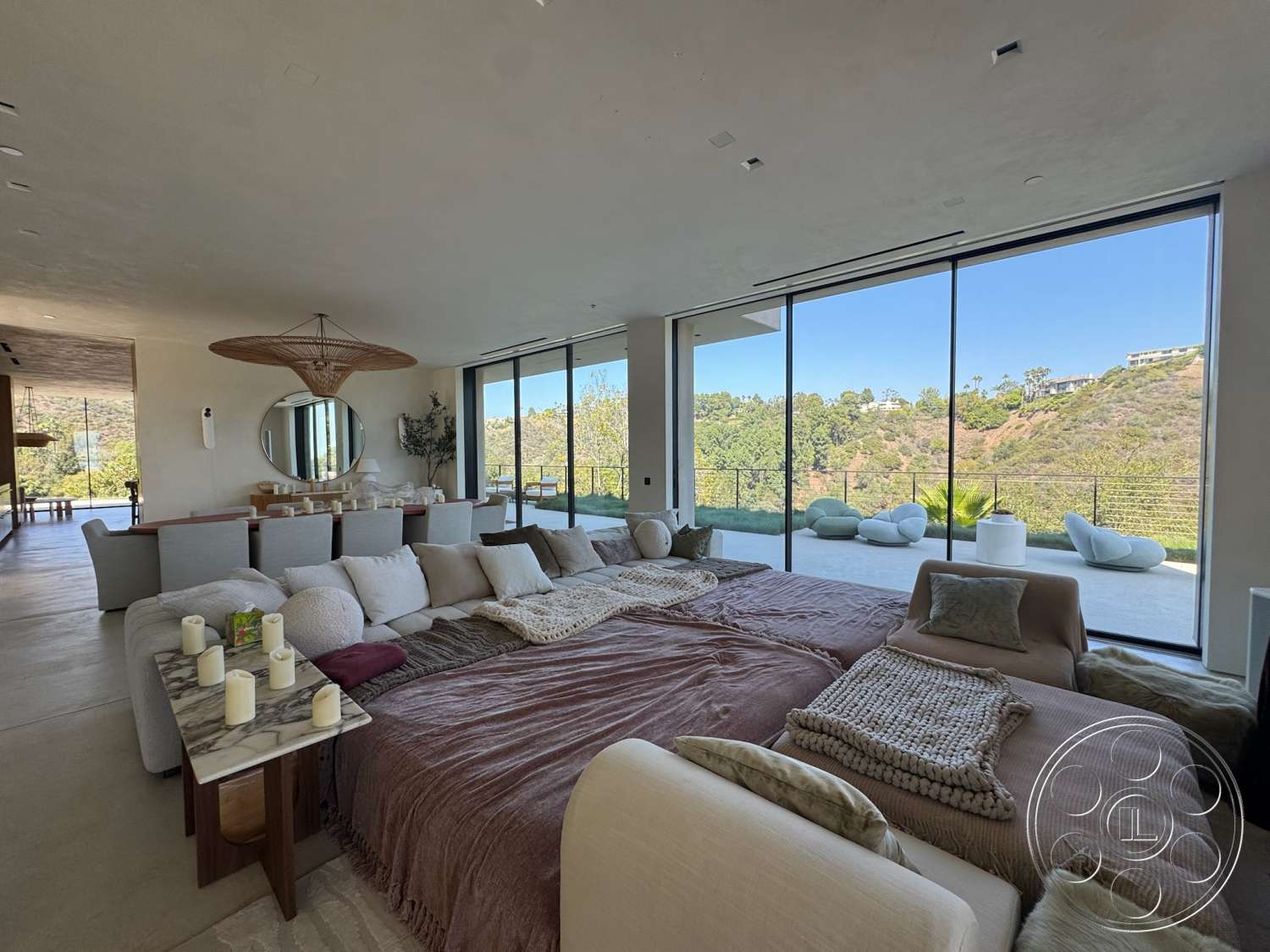 Modern 527 - natural light, contemporary style, concrete flooring, minimalist furniture, floor-to-ceiling windows, open concept living space, textured plaster walls, large sectional sofa, outdoor patio view, woven rattan light fixture, neutral fabric cushions, round mirror wall accent, decorative throws and blankets, green hillside setting