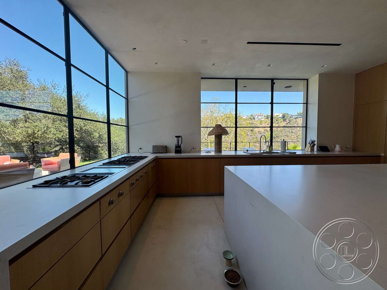 Modern 527 - floor-to-ceiling windows, modern kitchen island, stainless steel kitchen appliances, natural light-filled space, textured plaster wall finish, open-concept kitchen design, white quartz kitchen countertops, minimalist kitchen layout, panoramic hillside view, wood kitchen cabinetry, concrete kitchen flooring, centralized gas cooktop