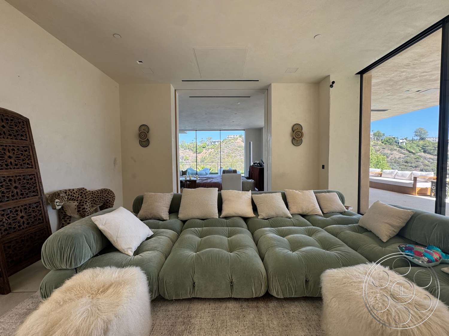 Modern 527 - natural light, minimalist design, textured area rug, modern furnishings, exposed ceiling, wood accent wall, open concept living space, contemporary architectural style, large floor-to-ceiling glass windows, wooden outdoor seating area, green tufted sofa, light beige stucco walls, cream decorative pillows, outdoor view of hillside