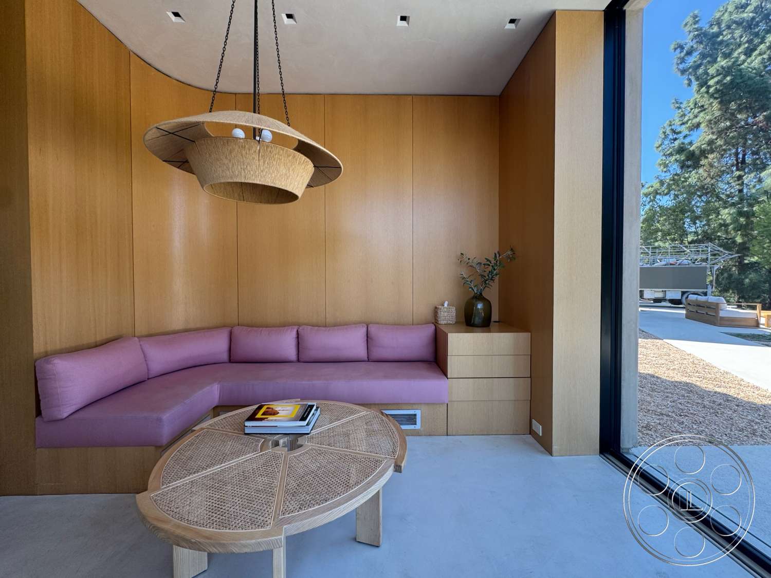 Modern 527 - large glass sliding doors, concrete floor, natural decor elements, custom built-in cabinetry, wood paneling walls, minimalist lighting fixture, plaster ceiling, pink upholstered bench seating, round rattan coffee table
