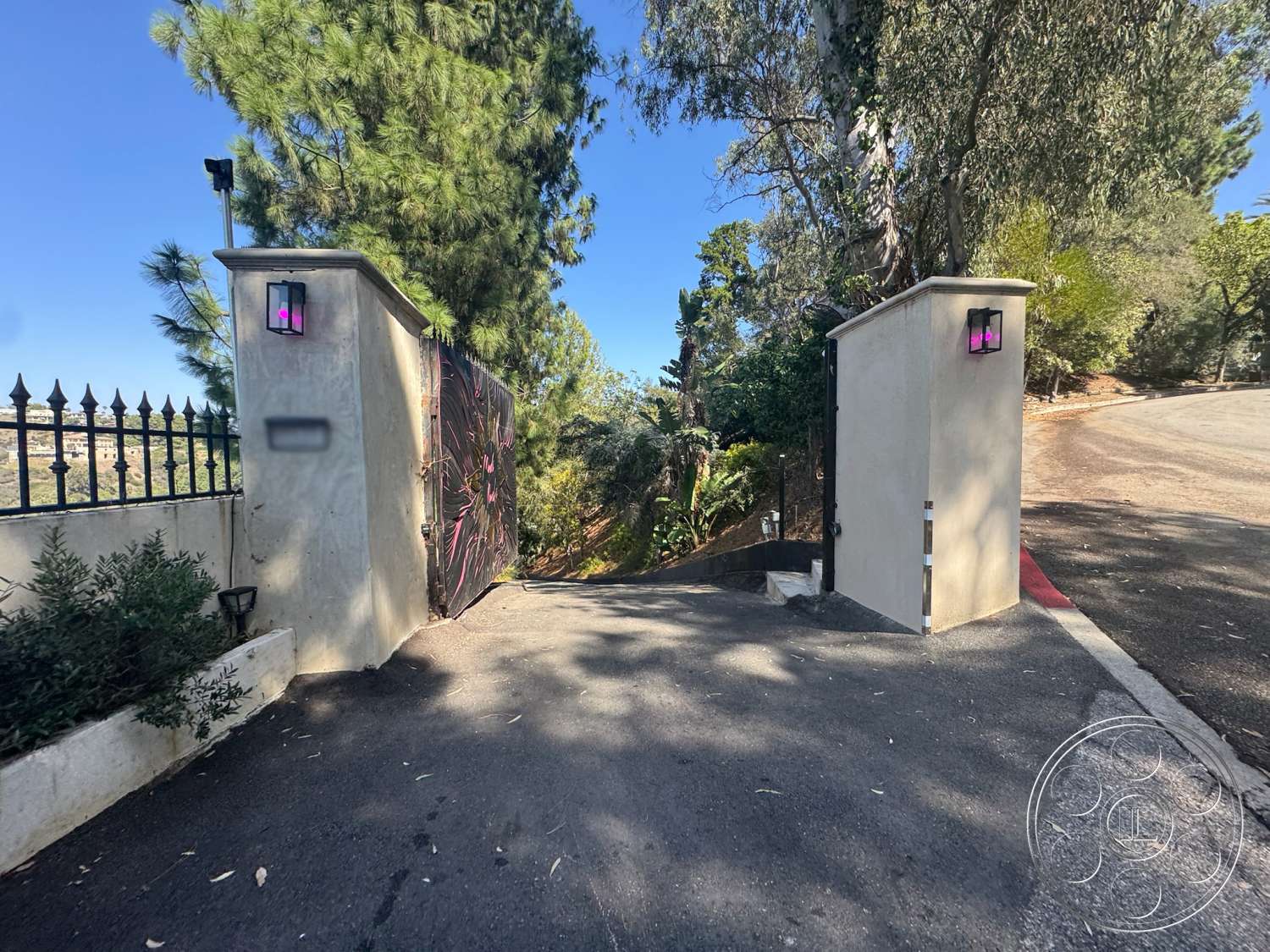 Modern 527 - exterior, sloped terrain, landscaped greenery, asphalt driveway, textured wall surface, tree-lined path, black wrought iron gate, mountain view setting, exterior lighting fixtures, concrete entrance gate pillars