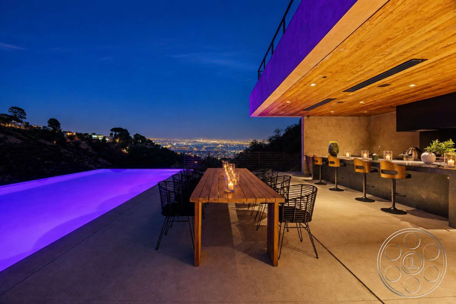 Modern 527 - exterior, wood dining table, city skyline view, modern kitchen island, metal outdoor chairs, concrete patio flooring, exposed wood ceiling, infinity pool with purple lighting, concrete bar counter, candlelit atmosphere