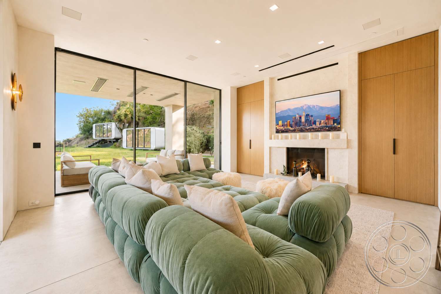 Modern 527 - neutral color palette, textured area rug, light wood cabinetry, floor-to-ceiling windows, modern wall-mounted TV, stone fireplace surround, smooth plaster walls, green upholstered sectional sofa, minimalist lighting fixtures, concrete living room floor, landscape view through large windows