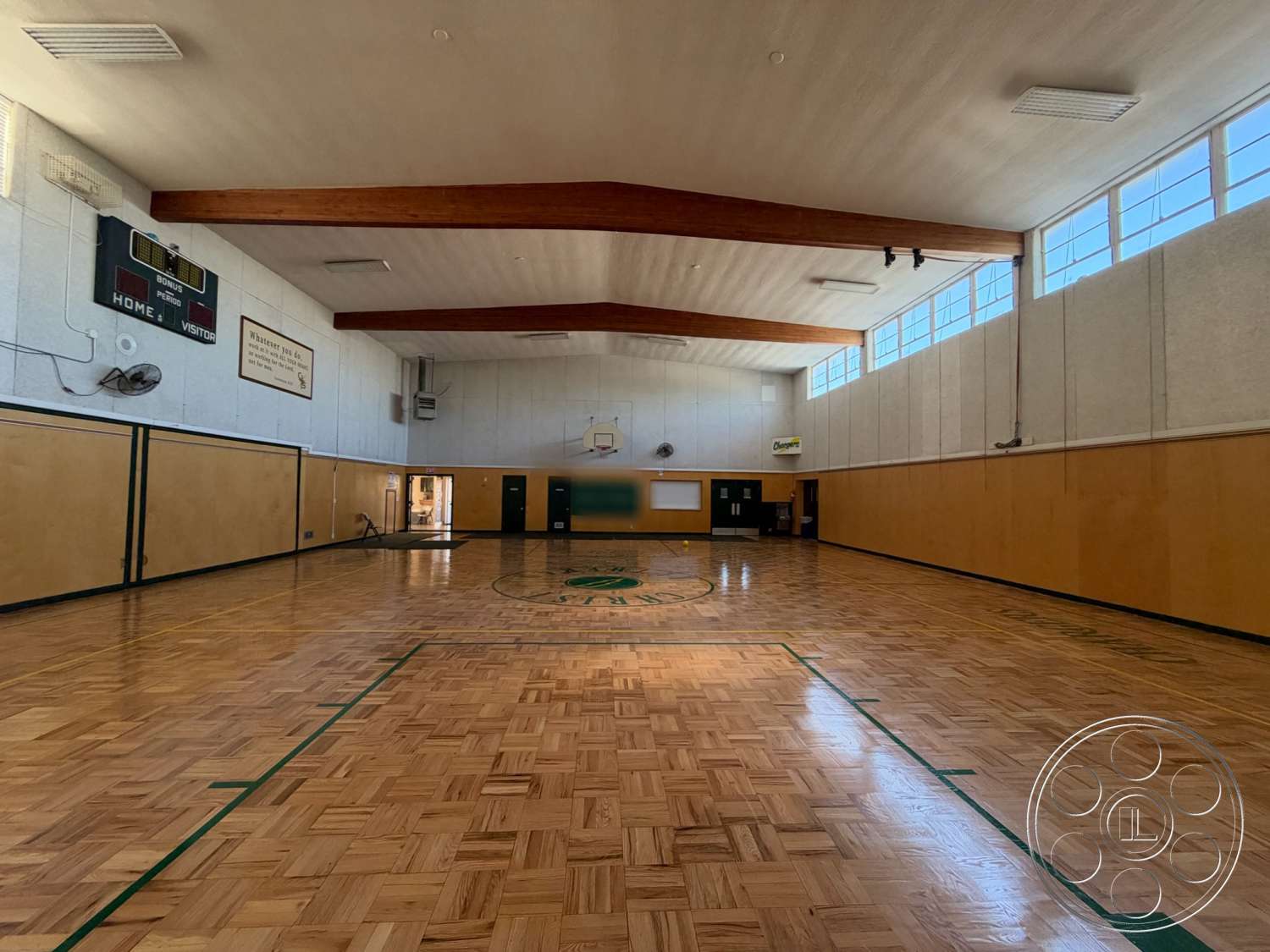 Community Center - wood parquet flooring, exposed wooden ceiling beams, painted plaster walls, basketball court markings, interior gymnasium, green trim details, windows with metal frames, scoreboard mounted on wall, wall-mounted air conditioning units, blackboard with wooden frame
