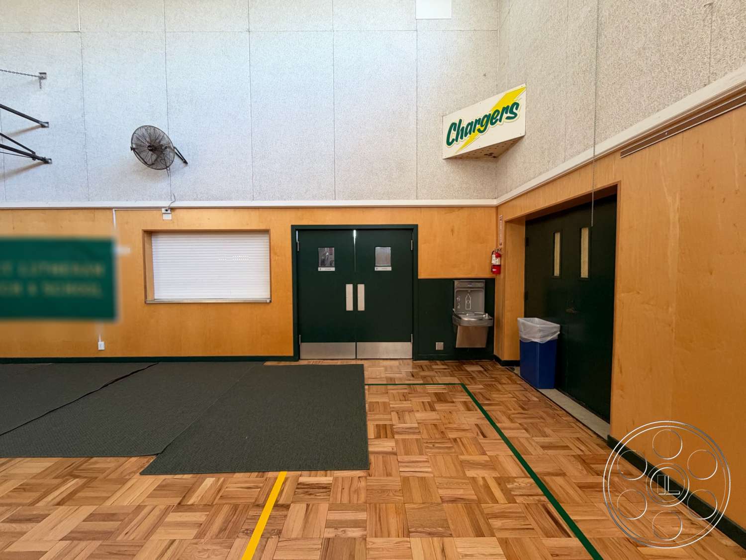 Community Center - exterior, wood paneling, ceiling fan, high ceiling, textured plaster walls, water fountain, floating wood floor, parquet floor pattern, green double doors, yellow court lines, signage with logo