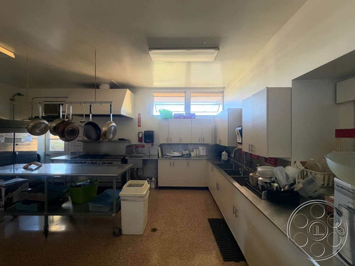 Community Center - large windows, terrazzo flooring, white cabinetry, open kitchen layout, interior kitchen, ample natural light, stainless steel countertop, commercial kitchen appliances, industrial kitchen design, hanging pot rack