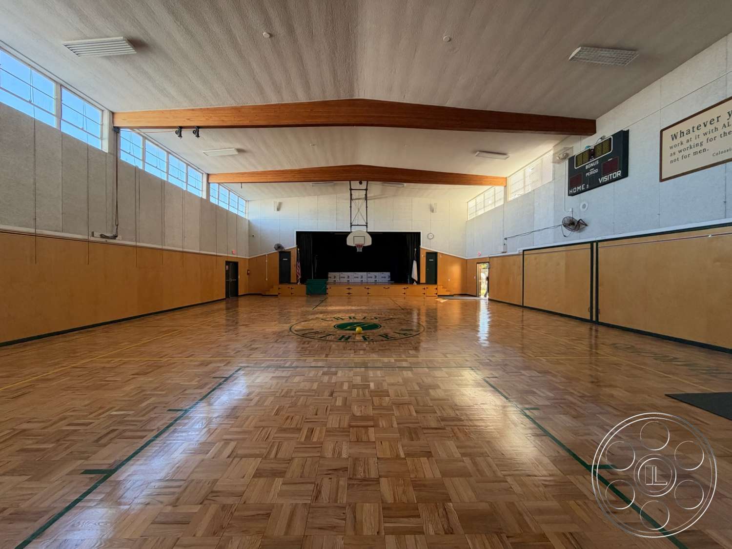 Community Center - black curtains, exposed wood ceiling beams, parquet wood flooring, open floor layout, smooth plaster walls, interior gymnasium, large vertical windows, wall-mounted scoreboard, yellow and green color accents, basketball hoop with hanging nets, dark wooden door, green painted wall borders, gymnasium seating area, entertainment signage