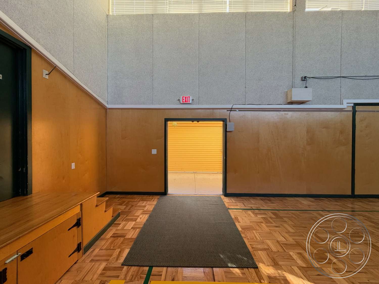 Community Center - parquet flooring, textured plaster wall treatment, glass door entrance, plywood wall panels, wood stair steps, rubber welcome mat, black door frames, light switch wall fixtures