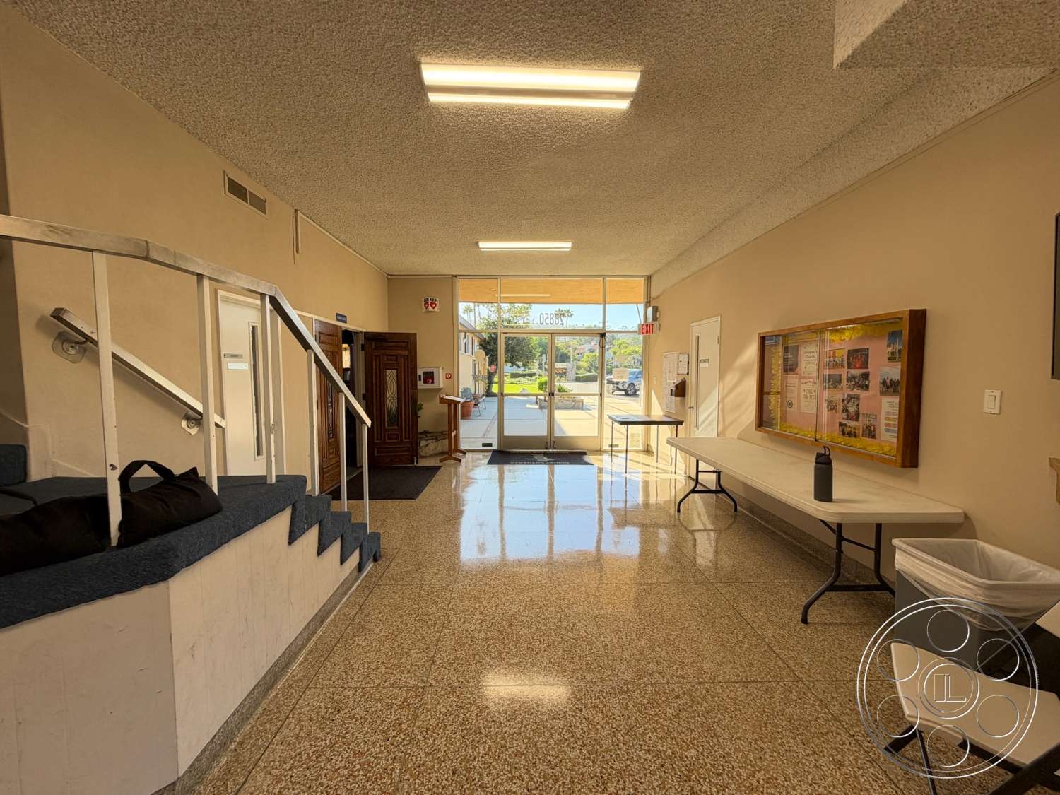 Community Center - terrazzo flooring, exposed ceiling, textured plaster walls, white painted walls, glass entrance door, metal handrails, wooden entrance door, open foyer area, built-in display case, accent wall with framed bulletin board