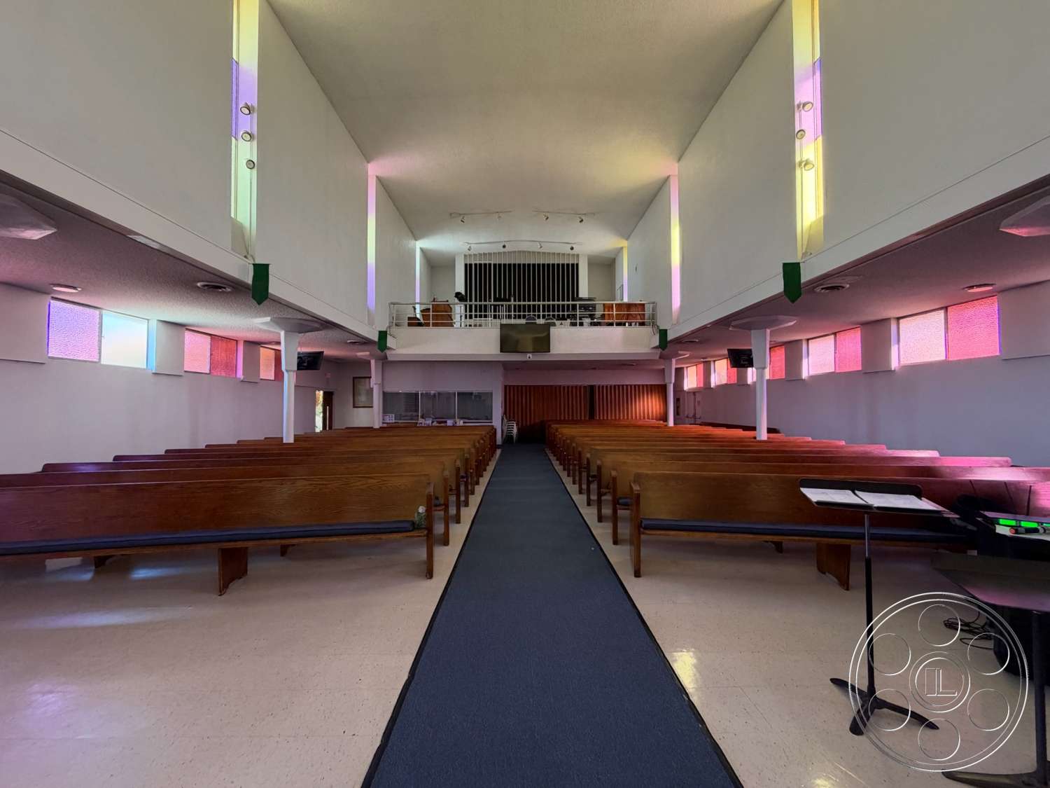 Community Center - spiral staircase, high vaulted ceiling, textured ceiling, stained glass windows, natural light from windows, audio-visual equipment, acoustic paneling, wooden pews, light-colored plaster walls, carpeted aisle, wooden stage, colored light accents, narrow aisle