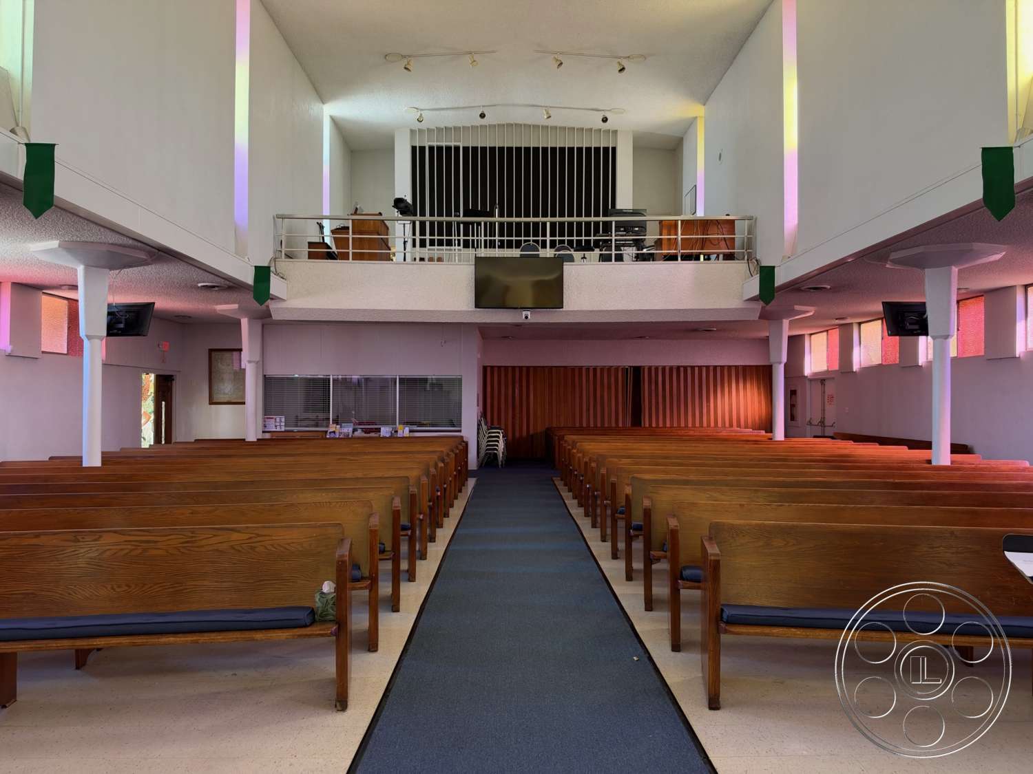 Community Center - polished concrete flooring, minimalist design elements, high vaulted ceiling, light beige walls, wood panel accent wall, glass wall panels, wooden pews, rectangular sanctuary layout, blue carpet runner, ceiling-mounted spotlights, simple railing balcony, colored light reflections