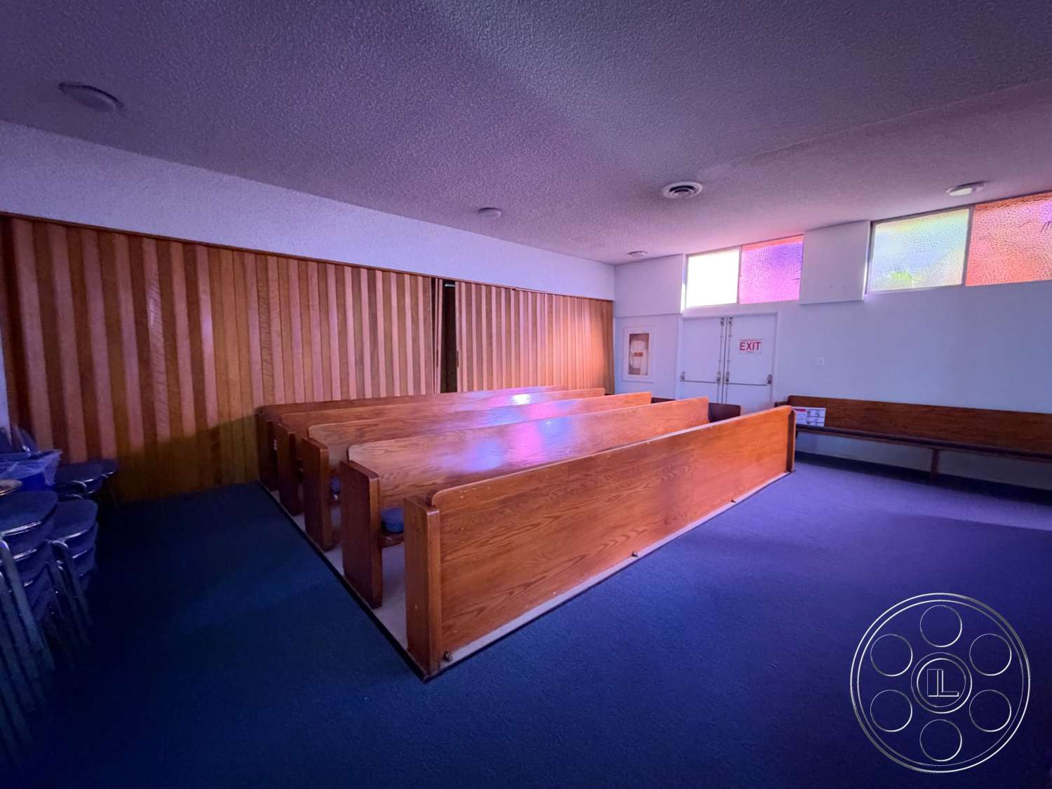 Community Center - carpet flooring, wooden bench seating, stained glass windows, suspended ceiling tiles, wood paneling walls, exit door, rectangular seating layout