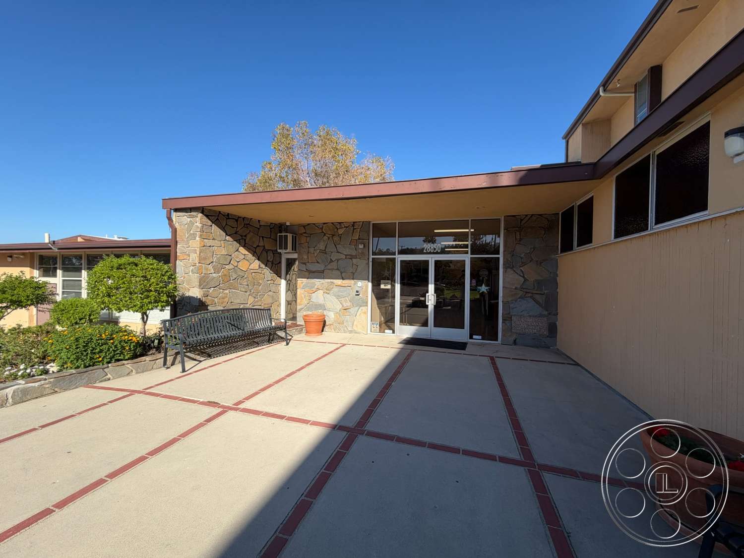 Community Center - exterior, stone accent wall, suburban setting, modern architectural style, concrete walkway, prominent windows, wooden planters, landscaped garden area, flat roof overhang, large glass entry doors, rectangular entrance, metal bench seating, brick border detail