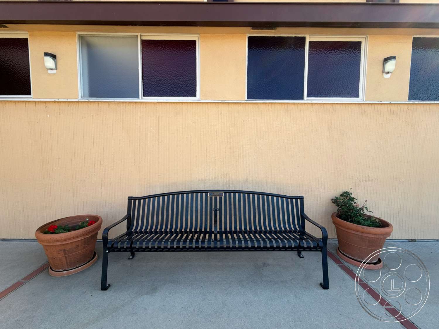 Community Center - exterior, green shrubbery, textured plaster walls, ceramic planter pots, concrete patio flooring, metal park bench, vertical rectangular windows, decorative red flowers