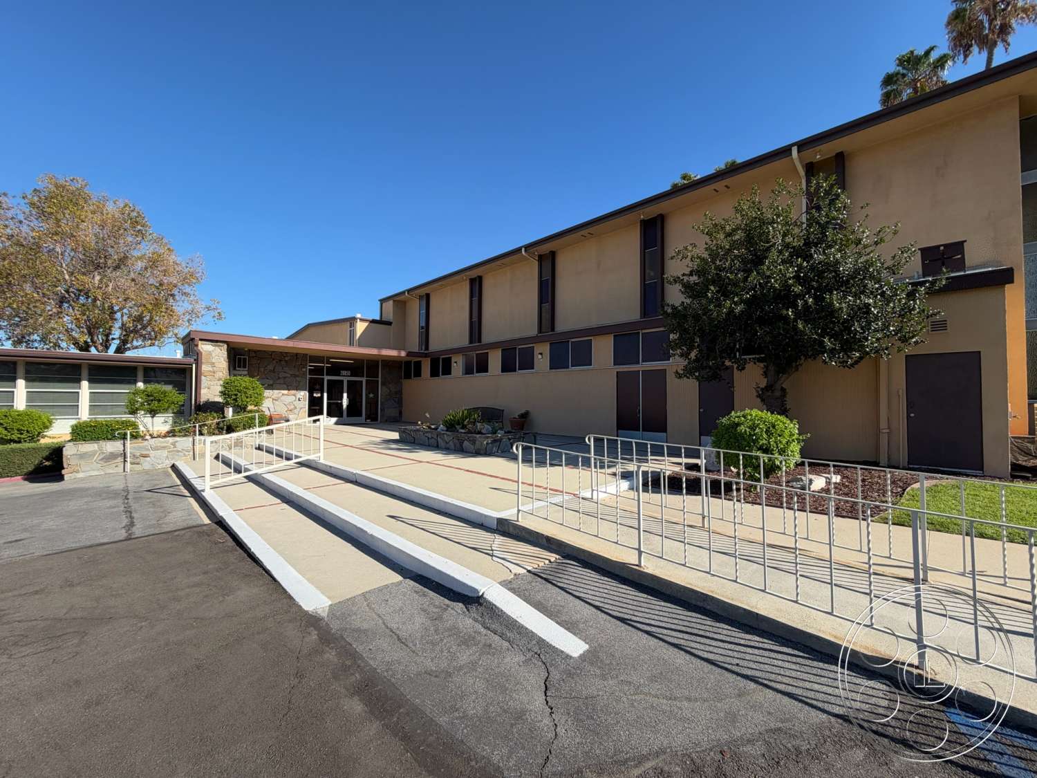 Community Center - large windows, exterior, stone accent wall, metal railings, landscaped front yard, concrete walkway, bush landscaping, asphalt parking lot, single-story building, flat roof structure, rectangular entryway, entrance ramp