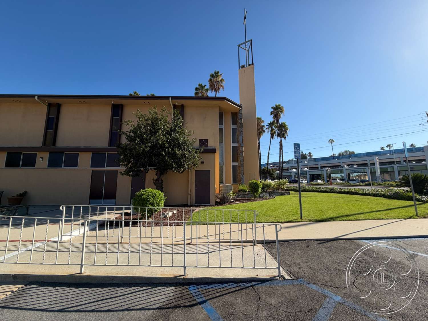 Community Center - large windows, exterior, flat roof, palm trees, metal railing, urban setting, landscaped front yard, grass lawn, paved walkway, stucco exterior, two-story building, stone feature wall, commercial property, concrete parking surface
