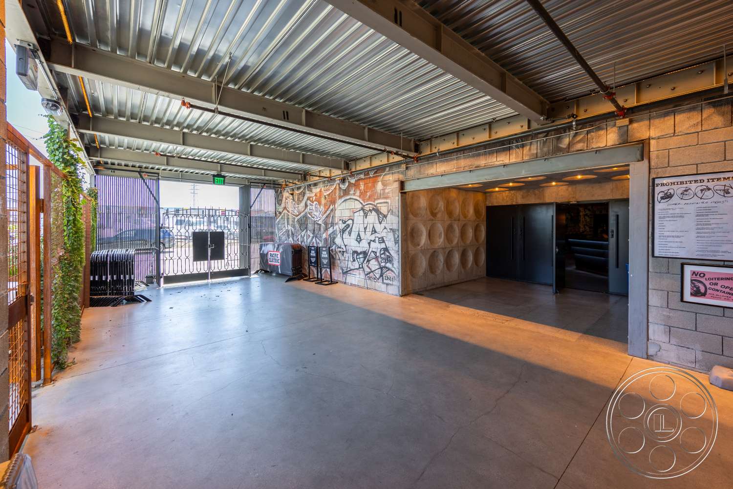 Club 74 - exterior, concrete floor, exposed concrete walls, urban setting, industrial design elements, graffiti wall art, open layout space, textured concrete accent wall, high ceilings with exposed beams, interior entrance, steel roofing panels, metal security gates, landscaped green walls