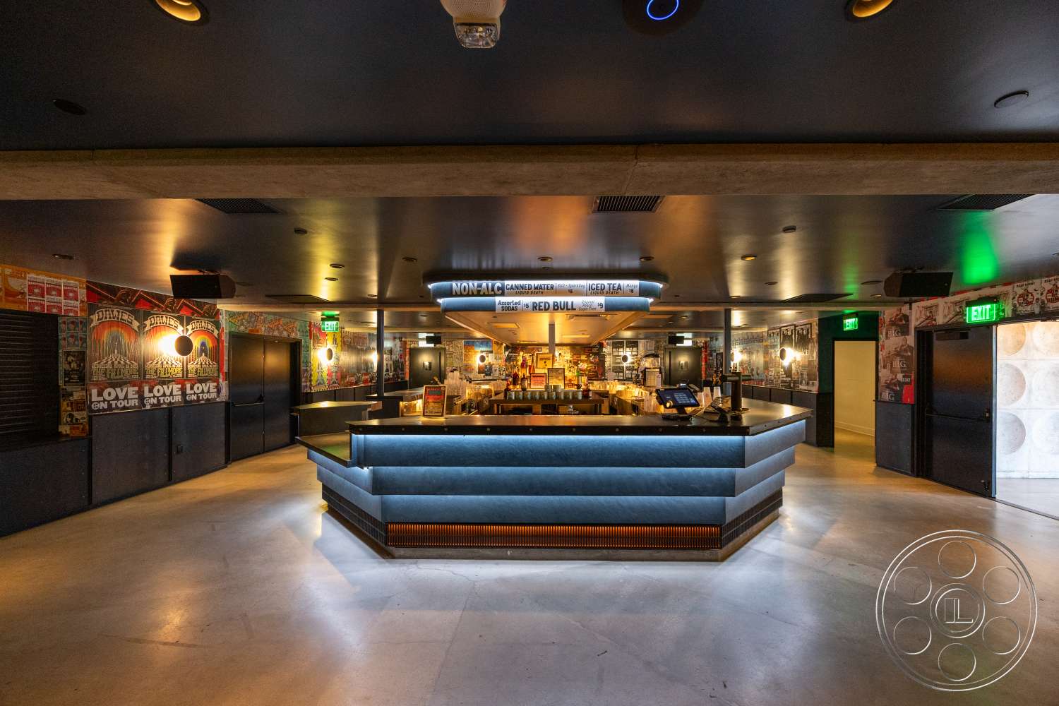 Club 74 - modern light fixtures, concrete flooring, vaulted ceiling, metal bar counter, recessed ceiling lights, exposed structural elements, wood paneling accent wall, dimmed lighting fixtures, black door frames, backlit bar surface, abstract wall artwork, ceiling-mounted speakers, colorful mural wallpaper, liquor display shelving