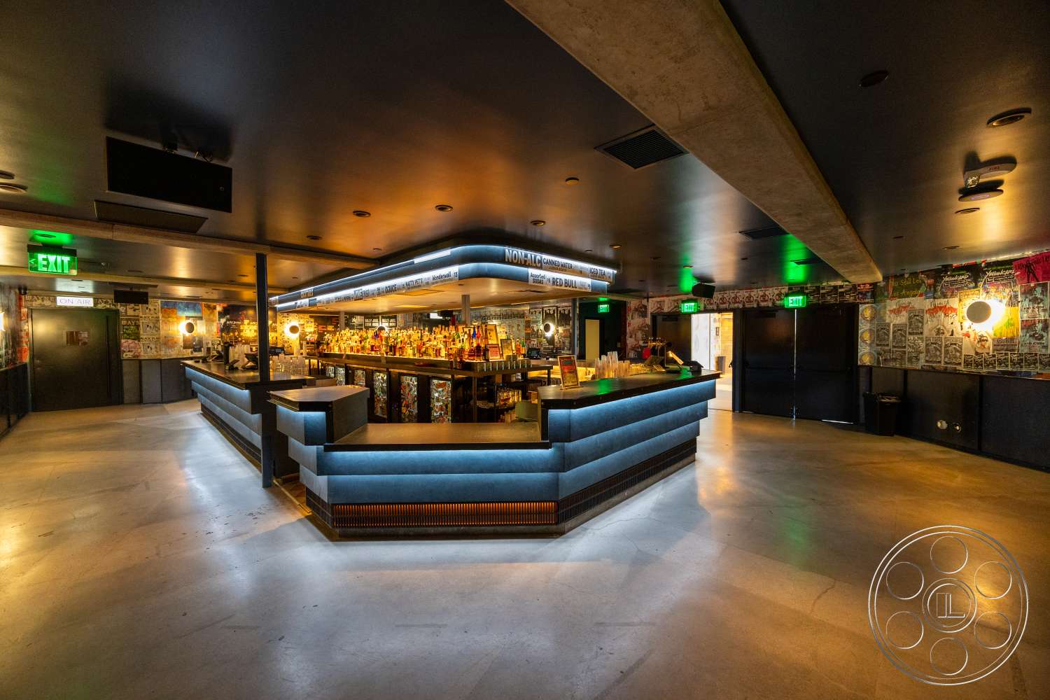 Club 74 - polished concrete floor, open floor plan, decorative wall art, black ceiling, ambient ceiling lighting, dimly lit atmosphere, curved bar counter, wood paneling bar front, exposed concrete structural beam, bottle display shelves, circular wall sconces