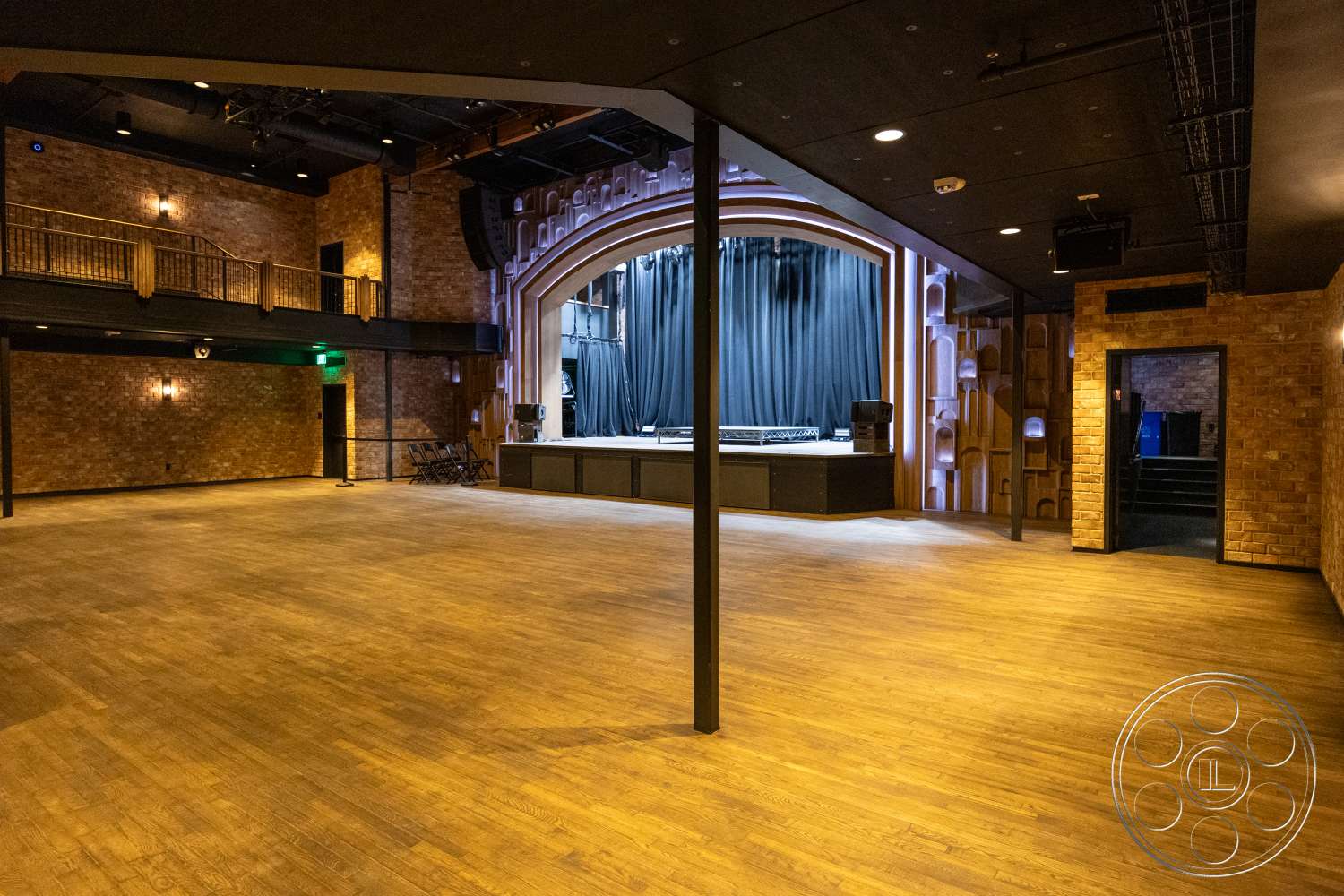 Club 74 - black ceiling, performance space, wooden stage flooring, brick accent walls, wooden railing balcony, theater room, arched proscenium stage, dim lighting fixtures, exposed structural support beams, auditorium design