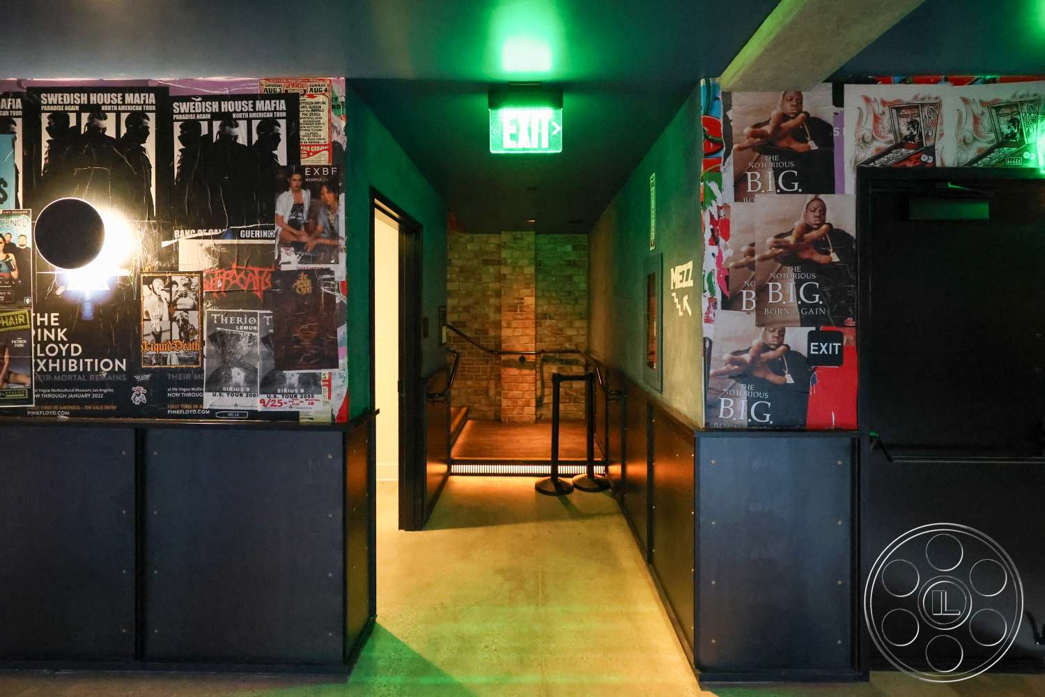 Club 74 - concrete floor, open space layout, metal railings, modern aesthetic, industrial style, dim lighting, narrow hallway, dark painted walls, exposed brick accent wall, exit signage, backlit signage, poster-covered wall
