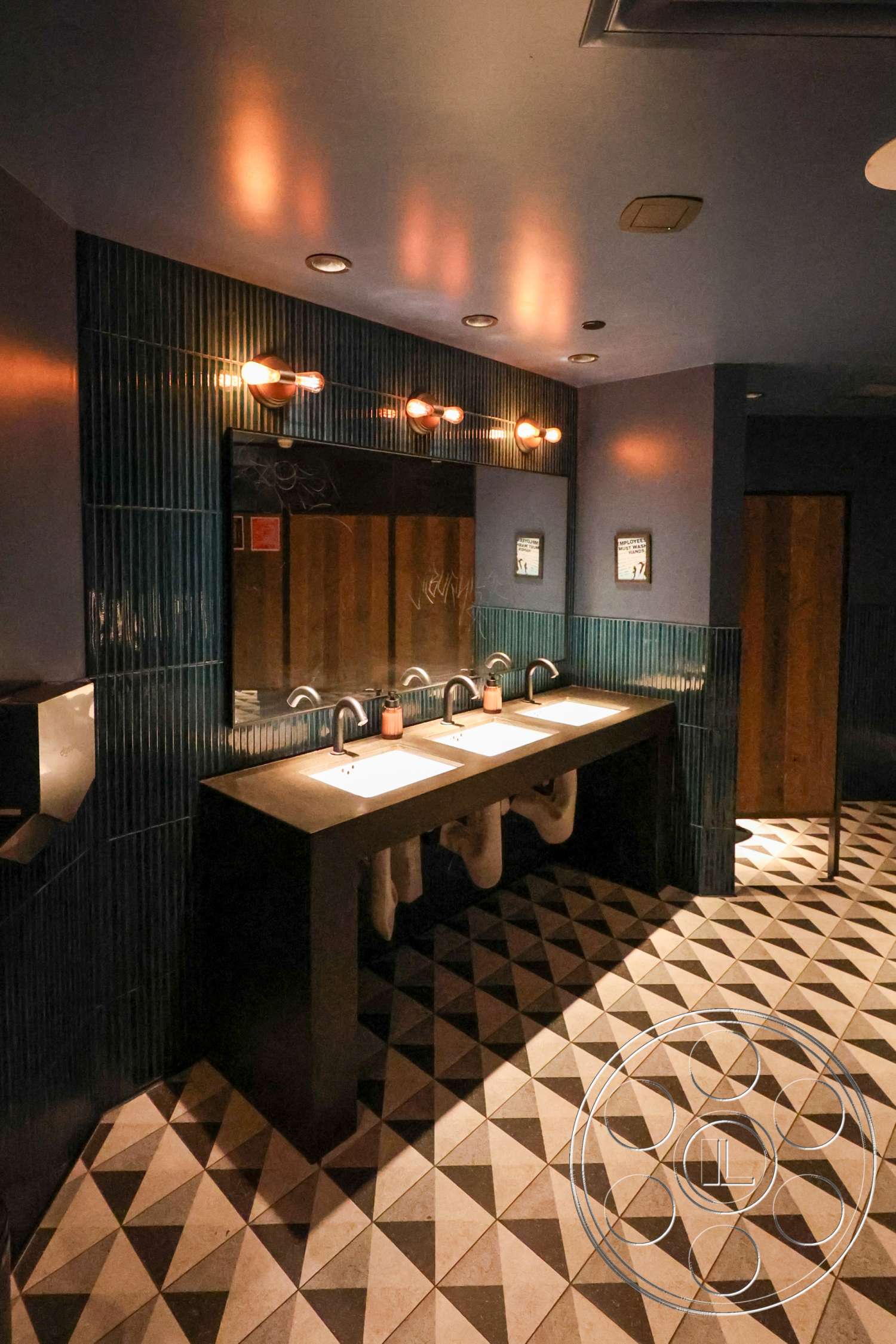 Club 74 - ambient lighting fixtures, interior bathroom, wall-mounted faucets, wooden door accents, modern sink design, concrete vanity top, textured blue ceramic wall tiles, geometric patterned floor tiles, triangular tile flooring, dark-colored cabinetry