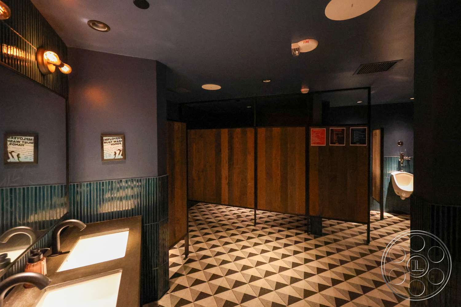 Club 74 - geometric tile flooring, industrial light fixtures, glossy black wall finish, textured blue wall tiles, striped ceramic wall tiles, hexagonal black and white floor tiles, wood panel bathroom stalls, modern wall-mounted sinks, brushed metal faucets, exposed ceiling with recessed lights, mirror above sink area