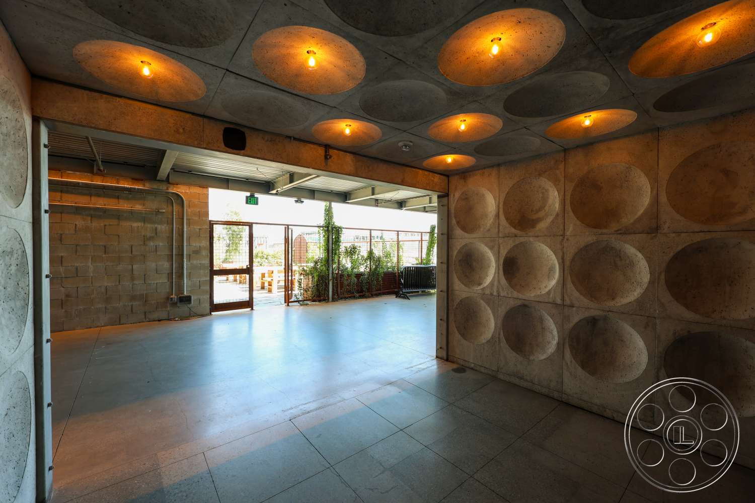 Club 74 - natural light, polished concrete flooring, exposed concrete walls, industrial lighting fixtures, exposed piping, floor-to-ceiling glass doors, indoor plant accents, textured concrete ceiling, open layout space, decorative concrete paneling