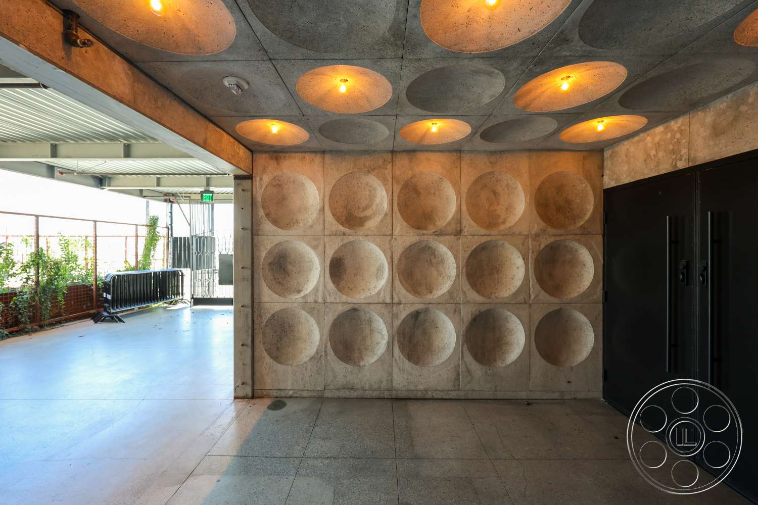 Club 74 - polished concrete flooring, exposed concrete walls, industrial style lighting fixtures, textured concrete ceiling with circular recesses, double black metal doors, interior entrance space