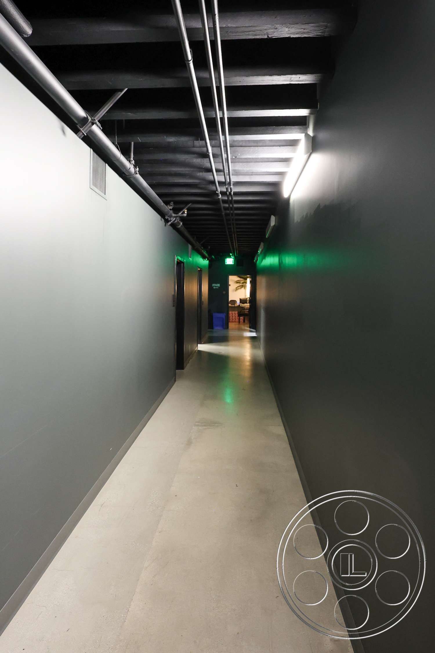 Club 74 - industrial light fixtures, exposed wood ceiling beams, dark painted walls, interior corridor, concrete hallway flooring, plumbing pipes along ceiling