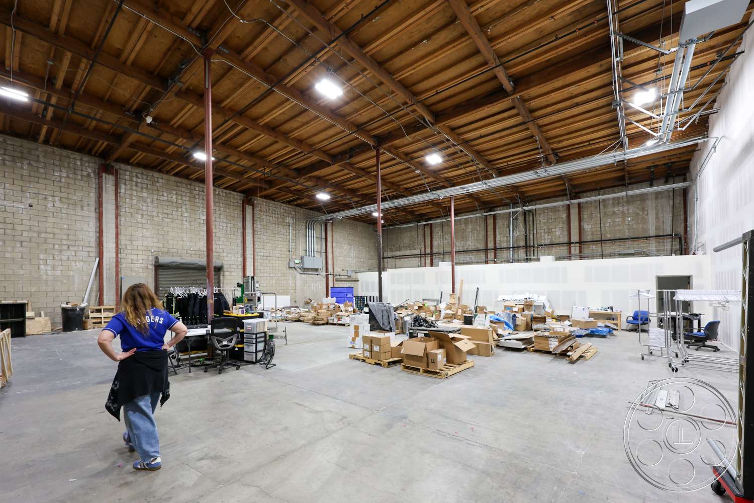 Club 74 - open floor plan, large open space, industrial lighting fixtures, storage area, exposed wood ceiling beams, exposed steel columns, concrete warehouse floor, block wall construction, workstation setup, interior warehouse environment