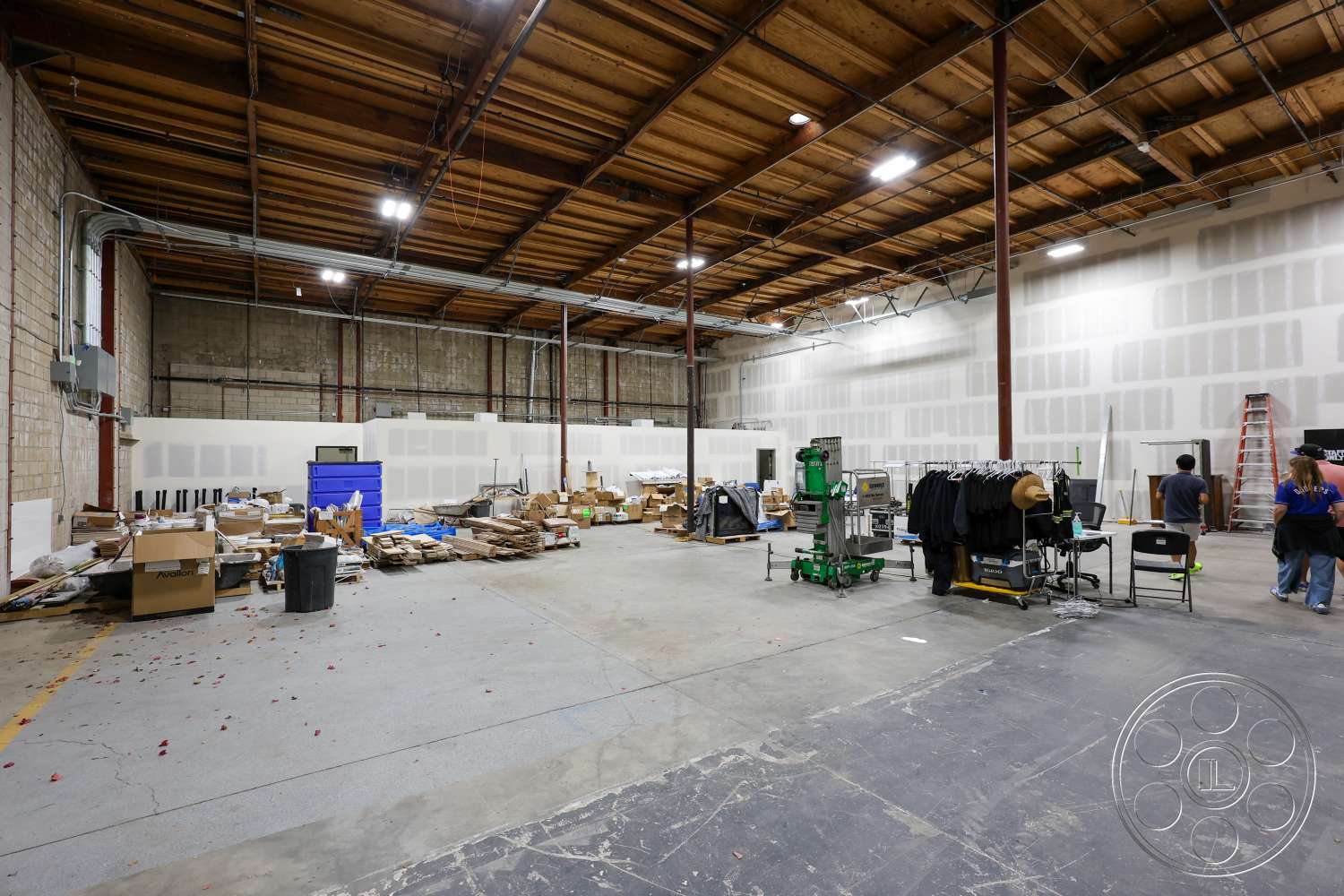 Club 74 - concrete flooring, metal shelving units, industrial lighting fixtures, workstation area, exposed wood ceiling beams, steel support columns, open floor layout, interior warehouse space, suspended electrical wiring, brick accent walls, unfinished drywall sections, storage boxes and materials
