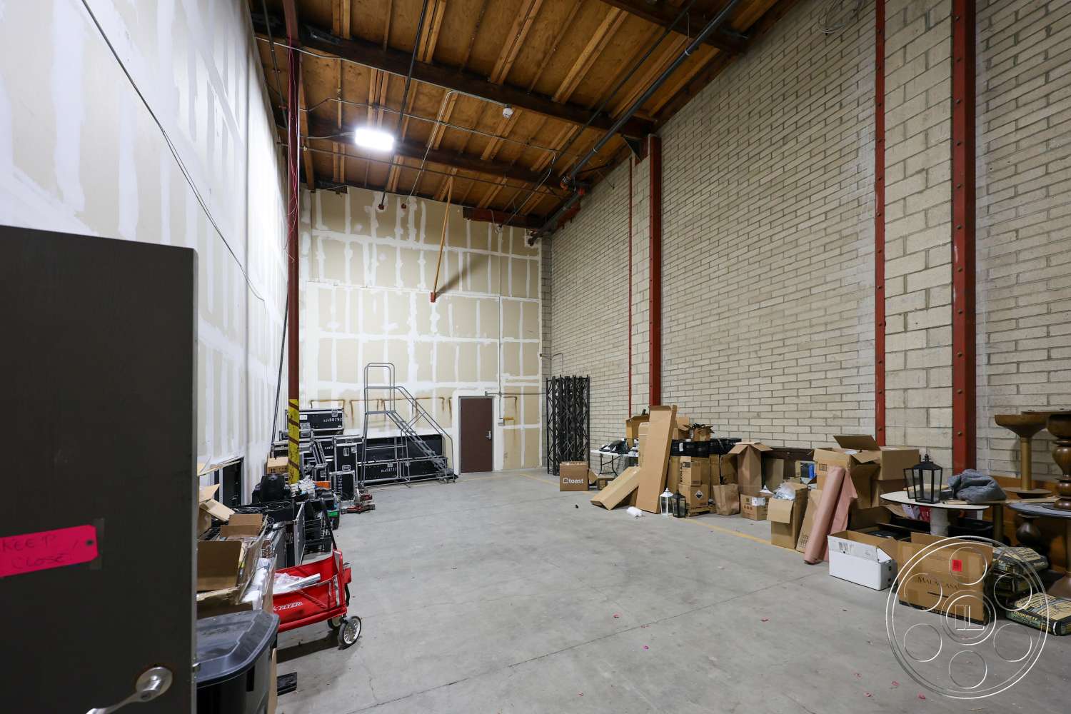 Club 74 - concrete floor, open space layout, warehouse style, brick wall, industrial lighting fixtures, storage area, exposed wood ceiling beams, drywall interior walls, steel structural supports