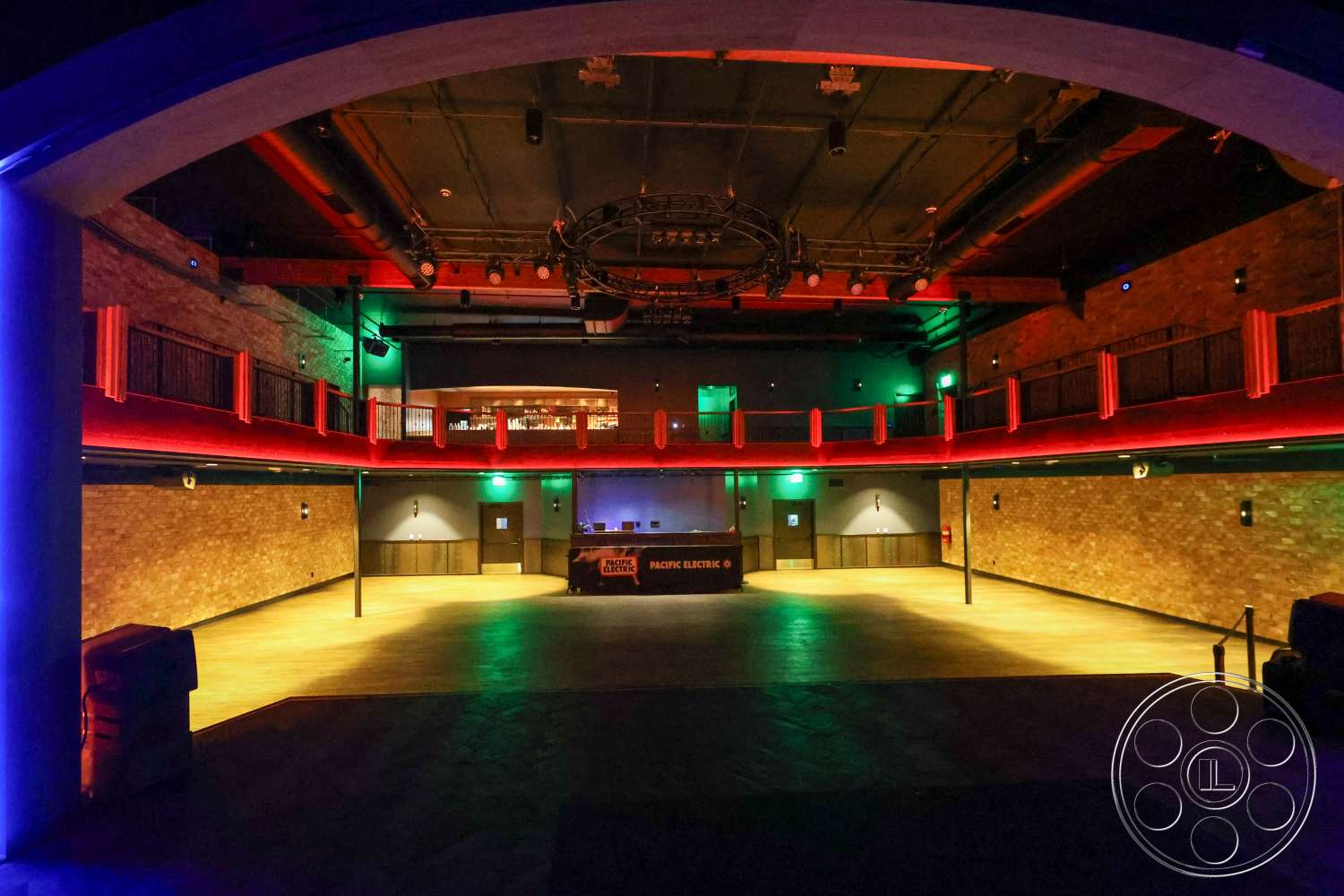 Club 74 - exposed brick walls, industrial lighting fixtures, red accent lighting, open performance space, metal ceiling beams, floor-to-ceiling height, hardwood dance floor, upper balcony seating, arcade-style bar area