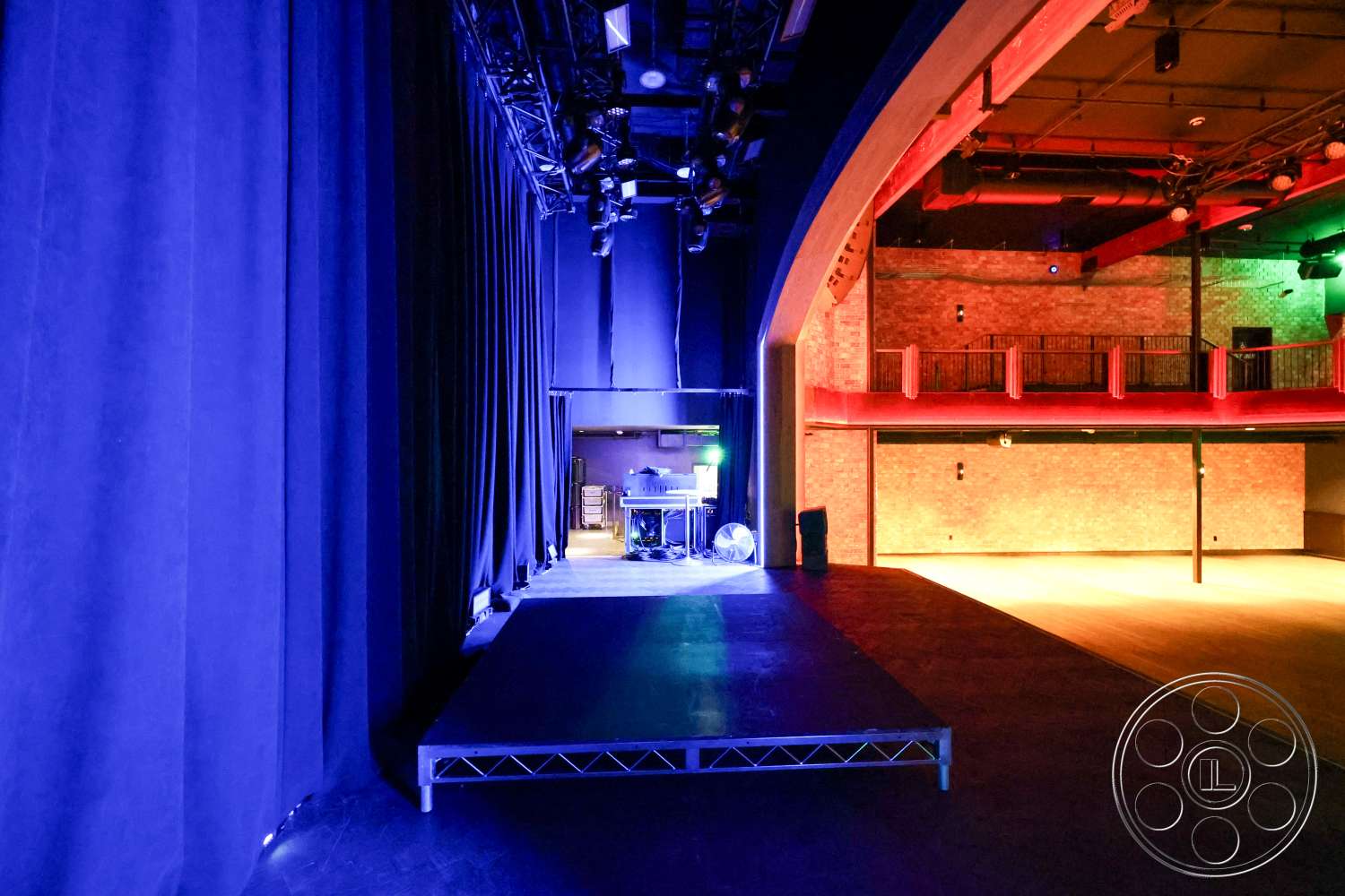 Club 74 - exposed brick wall, performance space, black flooring, industrial-style architecture, metal lighting rig, theater interior, auditorium setting, velvet stage curtains, sound equipment area, stage platform, wood balcony railings, colorful stage lighting