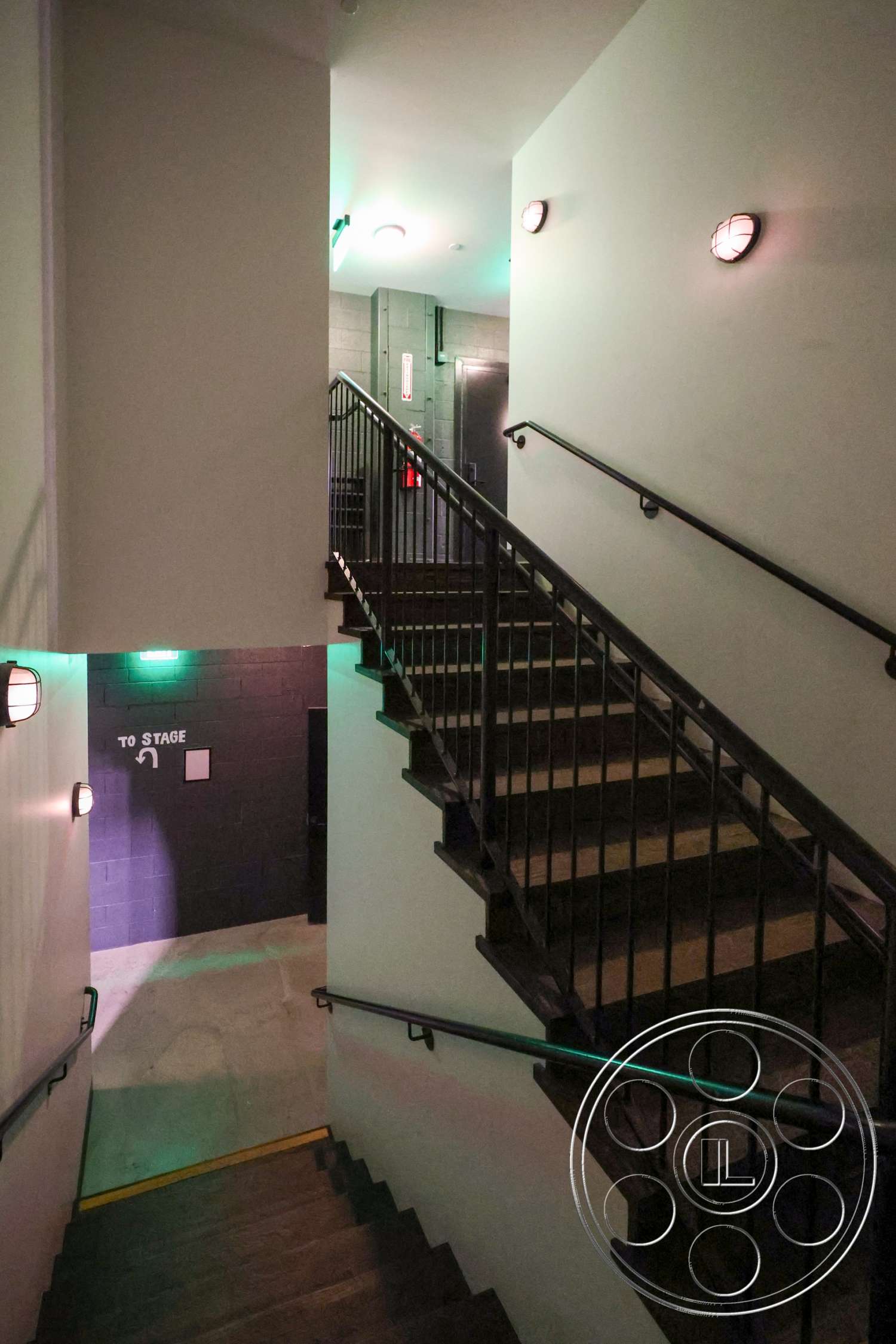 Club 74 - recessed lighting, concrete floor, exposed concrete wall, industrial lighting fixtures, wall sconces, white painted walls, metal stair railings, emergency exit signage, wooden staircase treads, yellow safety strip, stairwell
