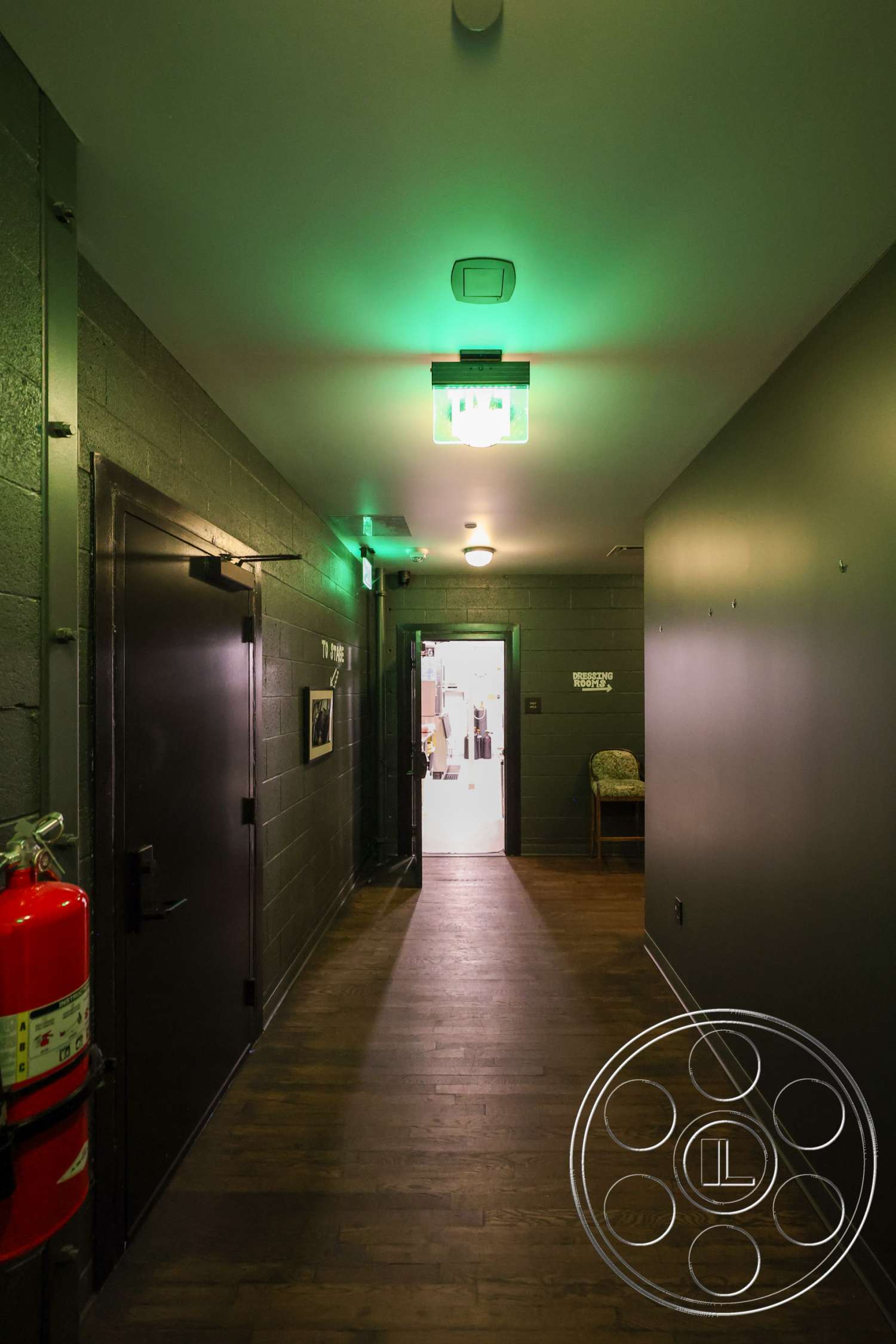 Club 74 - fire extinguisher, flush mount ceiling light, interior hallway, exposed concrete block walls, wood plank flooring, dark gray painted walls, emergency exit light fixture, black metal doors, green accent lighting