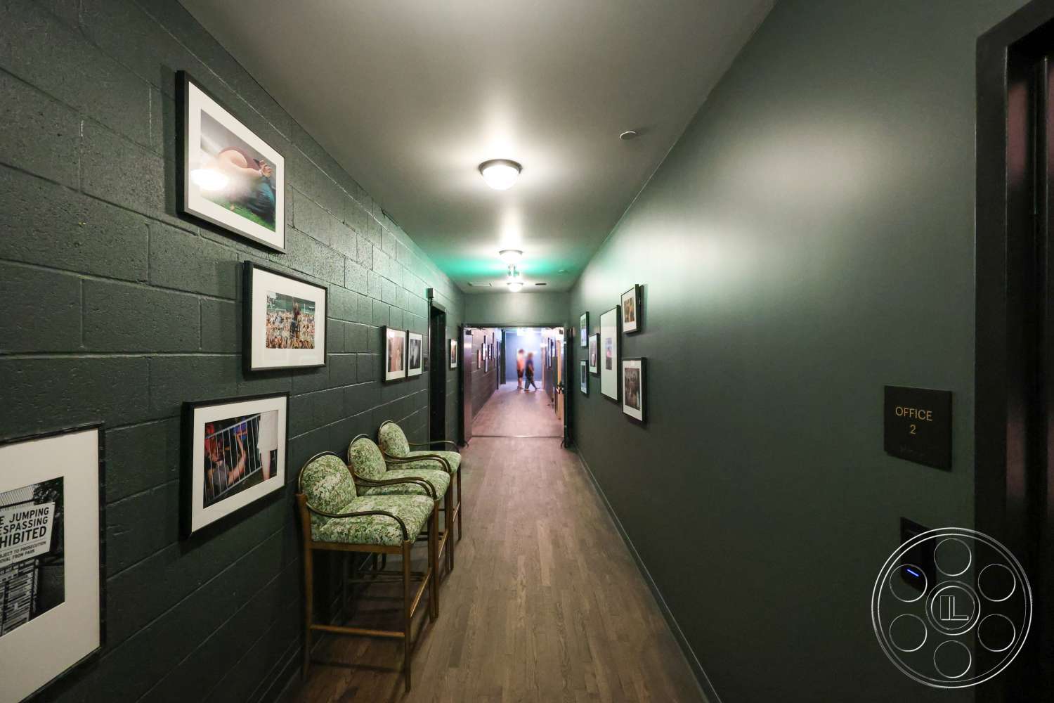 Club 74 - framed photographs on wall, interior hallway, modern door design, exposed concrete block walls, wood plank flooring, dark green painted walls, sconce lighting fixtures, wooden barstools with green upholstery, signage for office room