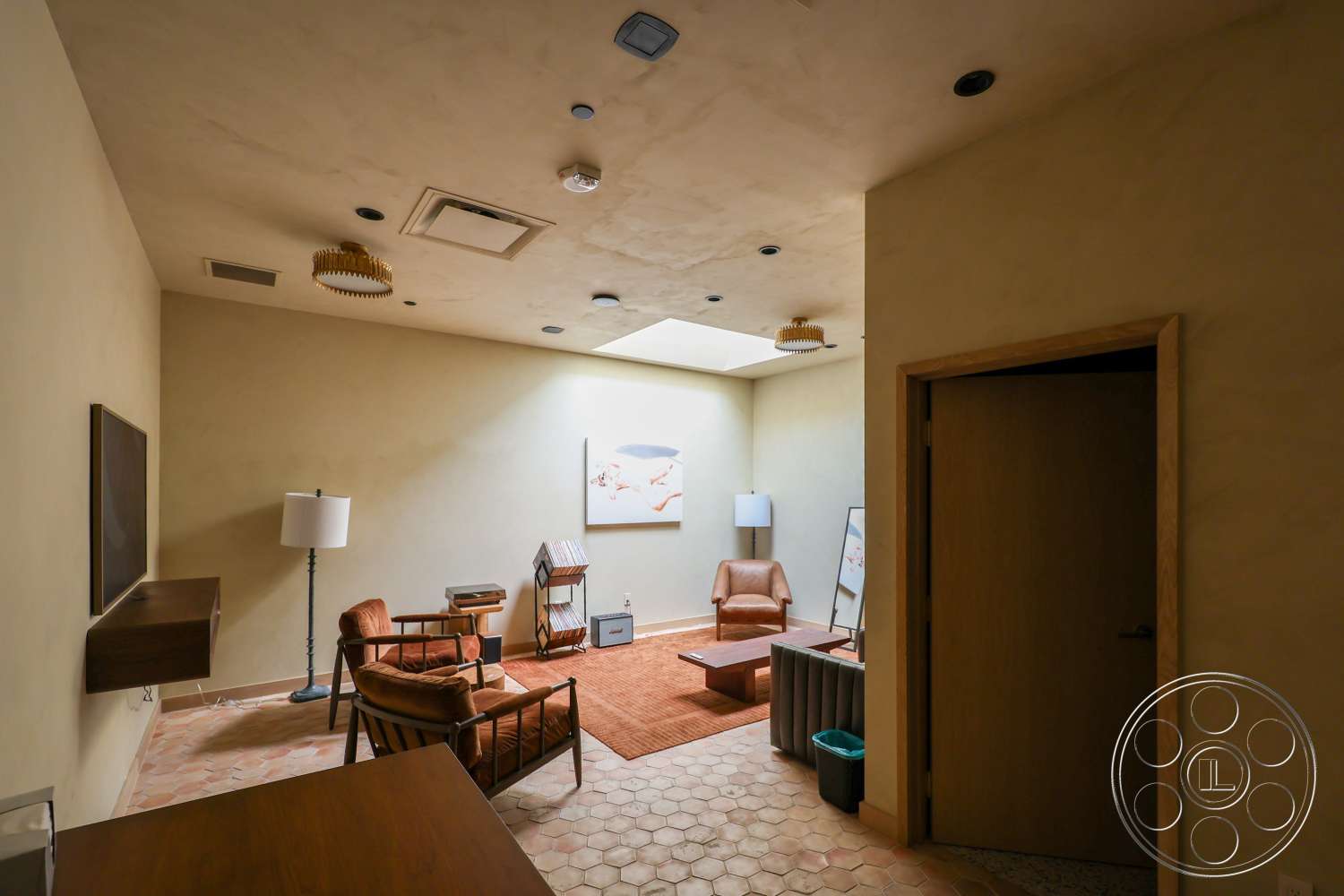 Club 74 - minimalist decor, neutral color palette, wooden accent chair, textured plaster walls, hexagonal tile flooring, skylight ceiling, wood panel door, modern living room lighting fixture, natural light infill
