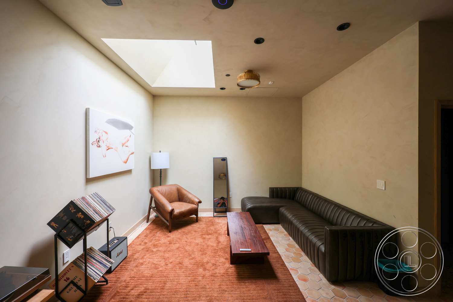 Club 74 - wood coffee table, plaster walls, framed wall art, soft natural lighting, dark wood trim, modern floor lamp, recessed ceiling lights, leather sectional sofa, hexagonal tile flooring, mid-century modern accent chair, skylight ceiling, terra cotta area rug, record storage rack