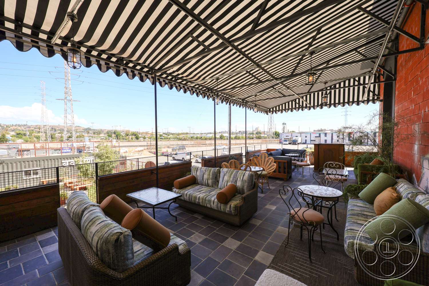 Club 74 - outdoor seating area, metal railing, landscaped greenery, concrete wall, wooden planter boxes, urban view, striped awning, accent pillows, metal lanterns, slate tile flooring, exterior patio area, woven rattan chairs, coffee tables with circular tops, semi-covered outdoor space