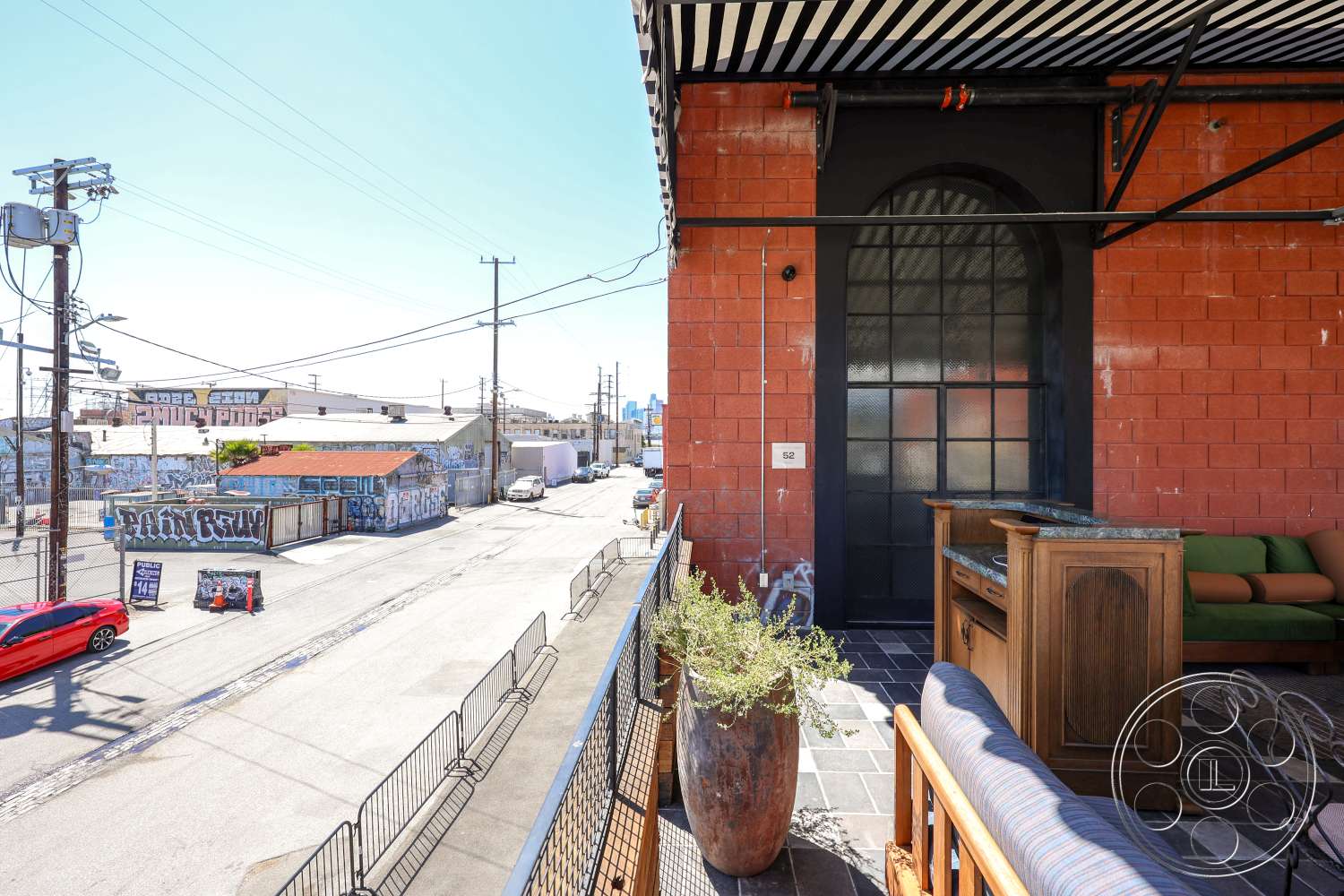 Club 74 - exterior, metal railing, power lines, striped awning, black framed glass door, graffiti wall, urban street view, tile patio flooring, red concrete block wall, wooden outdoor bar, green upholstered seating