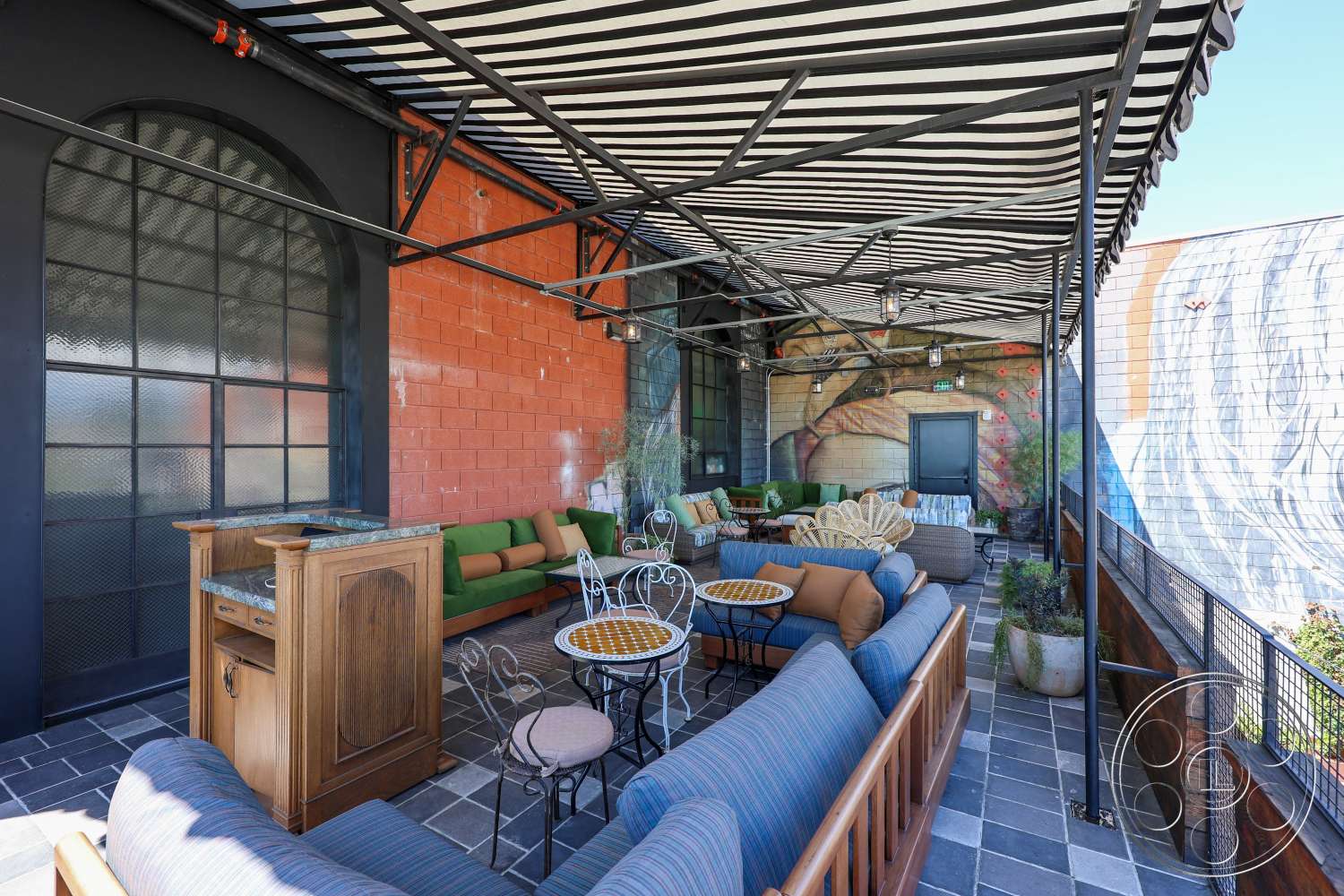 Club 74 - exterior, outdoor seating area, exposed brick wall, decorative planters, colorful mural, slate patio flooring, wooden bar countertop, modern lounge furniture, metal awning, glass paneled wall, metal framed furniture, striped outdoor fabric