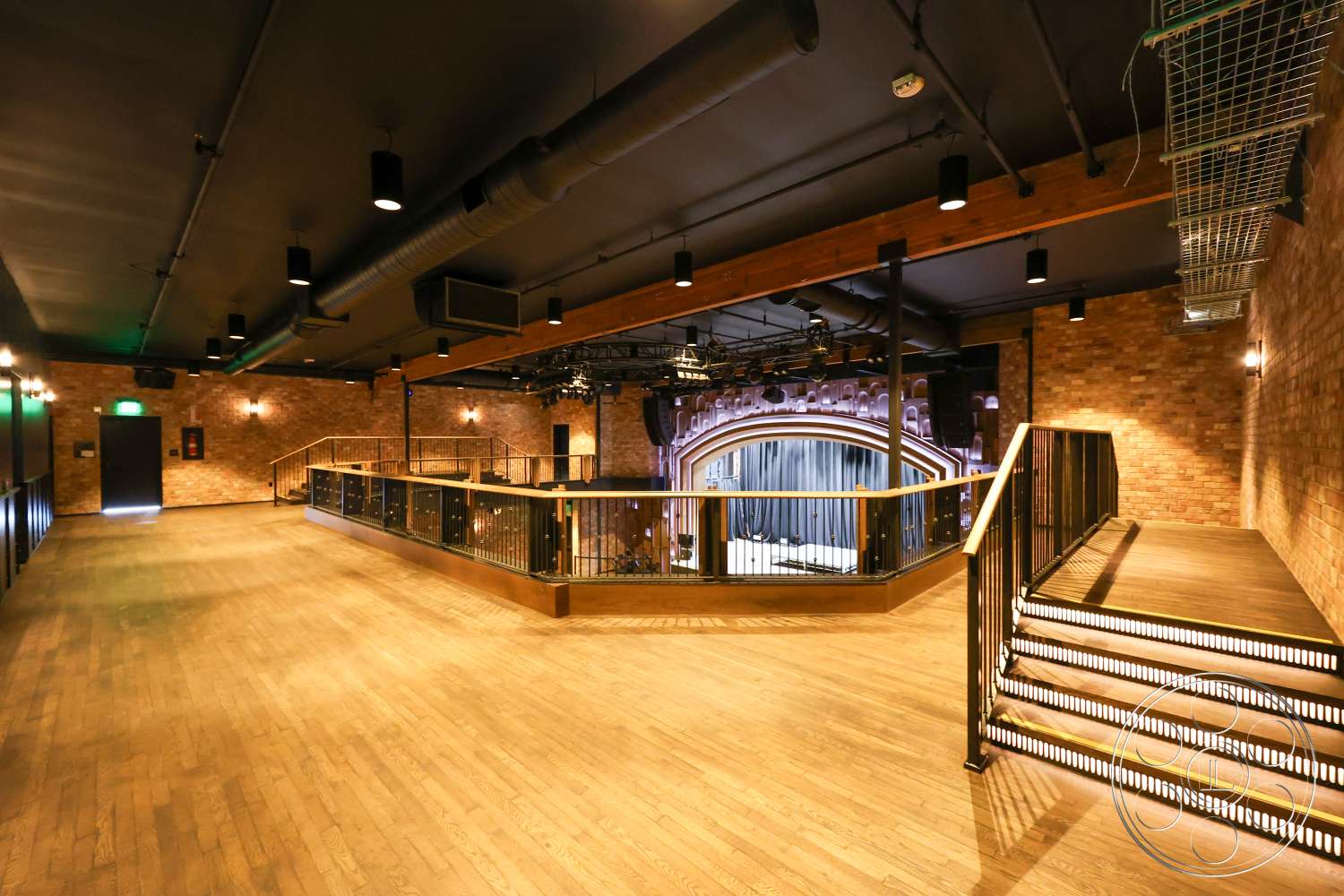 Club 74 - hardwood flooring, interior space, warm color palette, exposed brick walls, industrial lighting fixtures, accent lighting, black metal railings, wood beam ceiling, open floor layout, stage area with theater curtains