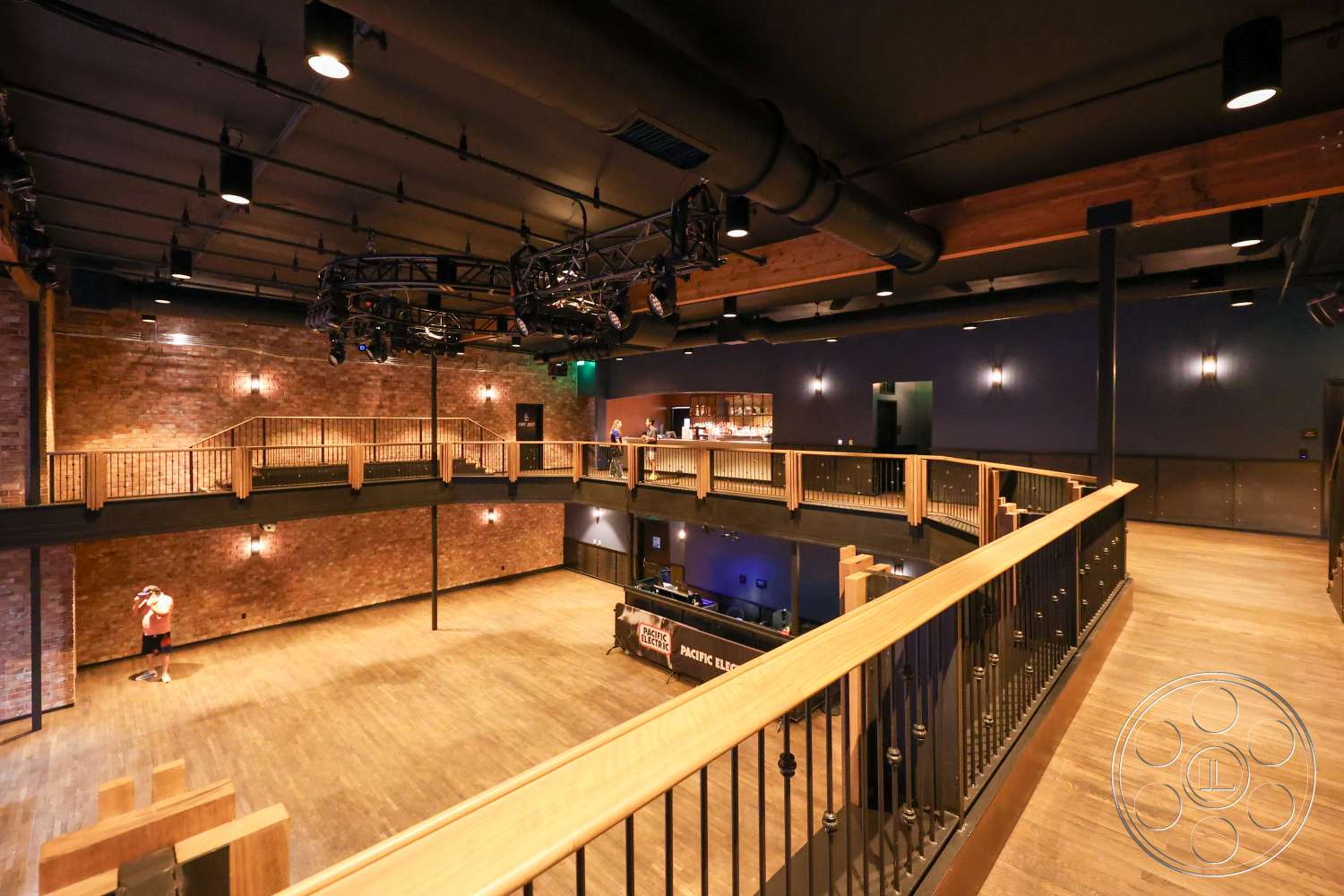 Club 74 - hardwood flooring, exposed brick walls, dark blue wall treatment, open performance space, black metal stair railings, wooden balcony railing, industrial ceiling with exposed piping, beam ceiling structure, spotlights lighting fixtures, interior venue space