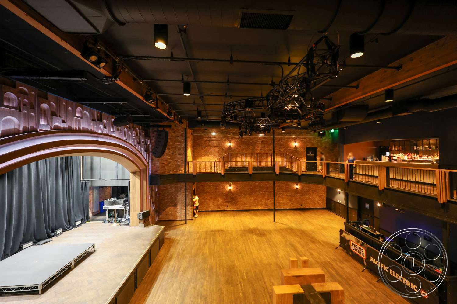 Club 74 - hardwood flooring, exposed ductwork, wood beam ceiling, exposed brick accent wall, open interior space, industrial style elements, black stage with raised platform, suspended lighting grid, arched wooden stage proscenium, bar area with wooden counter, balcony with wooden railing, theater room interior