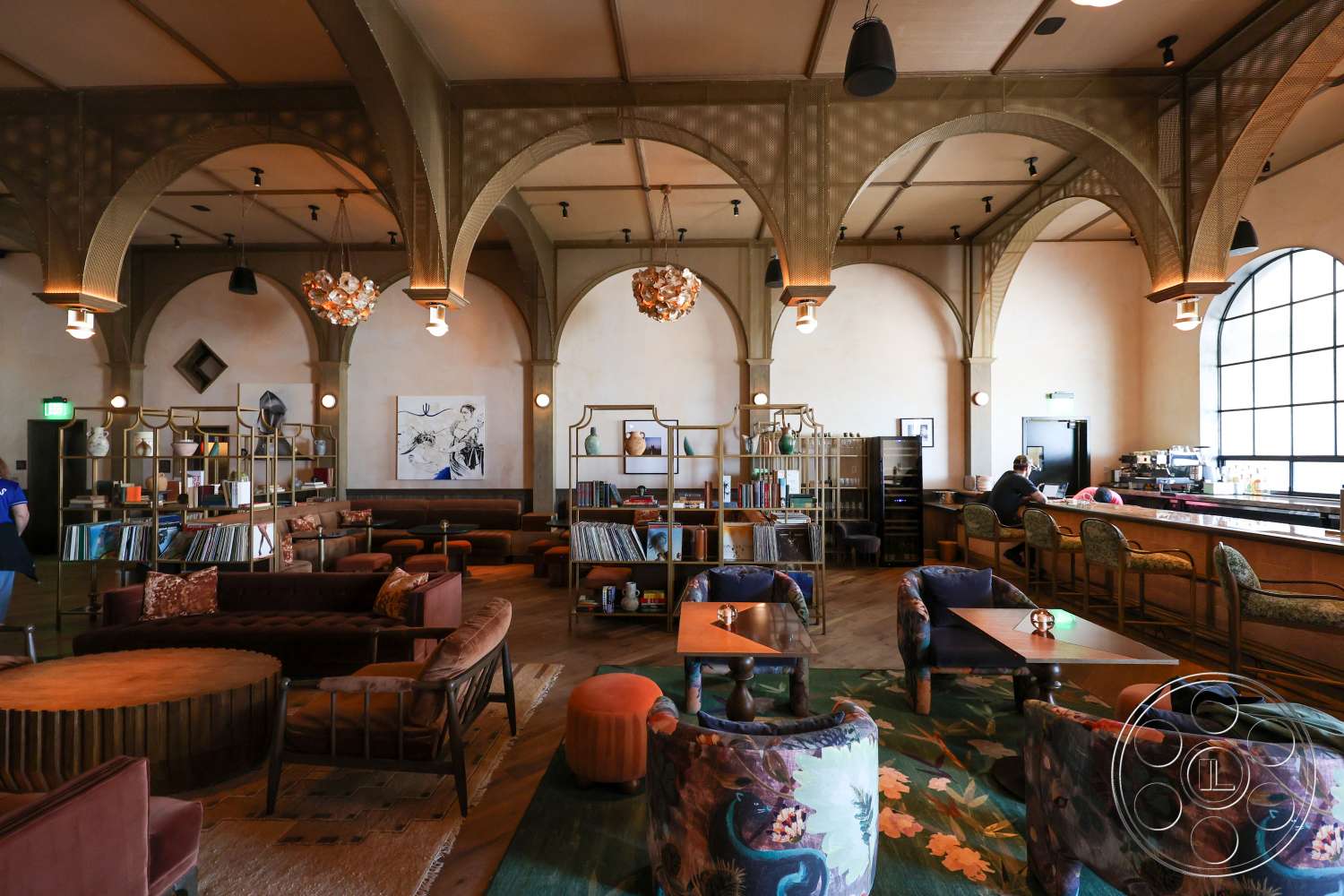 Club 74 - hardwood flooring, textured plaster walls, large arched windows, exposed wooden ceiling beams, modern chandelier lighting, curved velvet sofas, round wooden coffee tables, arched ceiling architecture, library shelving units with decorative objects, vintage-style bar counter, open social lounge area