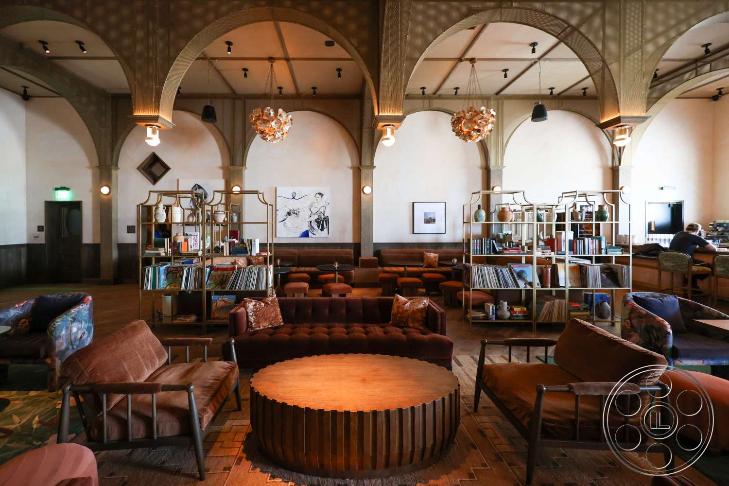 Club 74 - neutral color palette, exterior, ambient lighting, comfortable seating, circular wooden coffee table, arched ceilings, modern art decor, upholstered sofa, designer pendant lighting, wood paneling walls, flush mount ceiling lights, open lounge area, woven textile armchairs, metal bookshelf, large wood floor tiles, library corner, polished wood floor